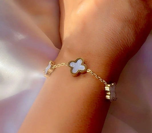 A gold chain bracelet with white clovers