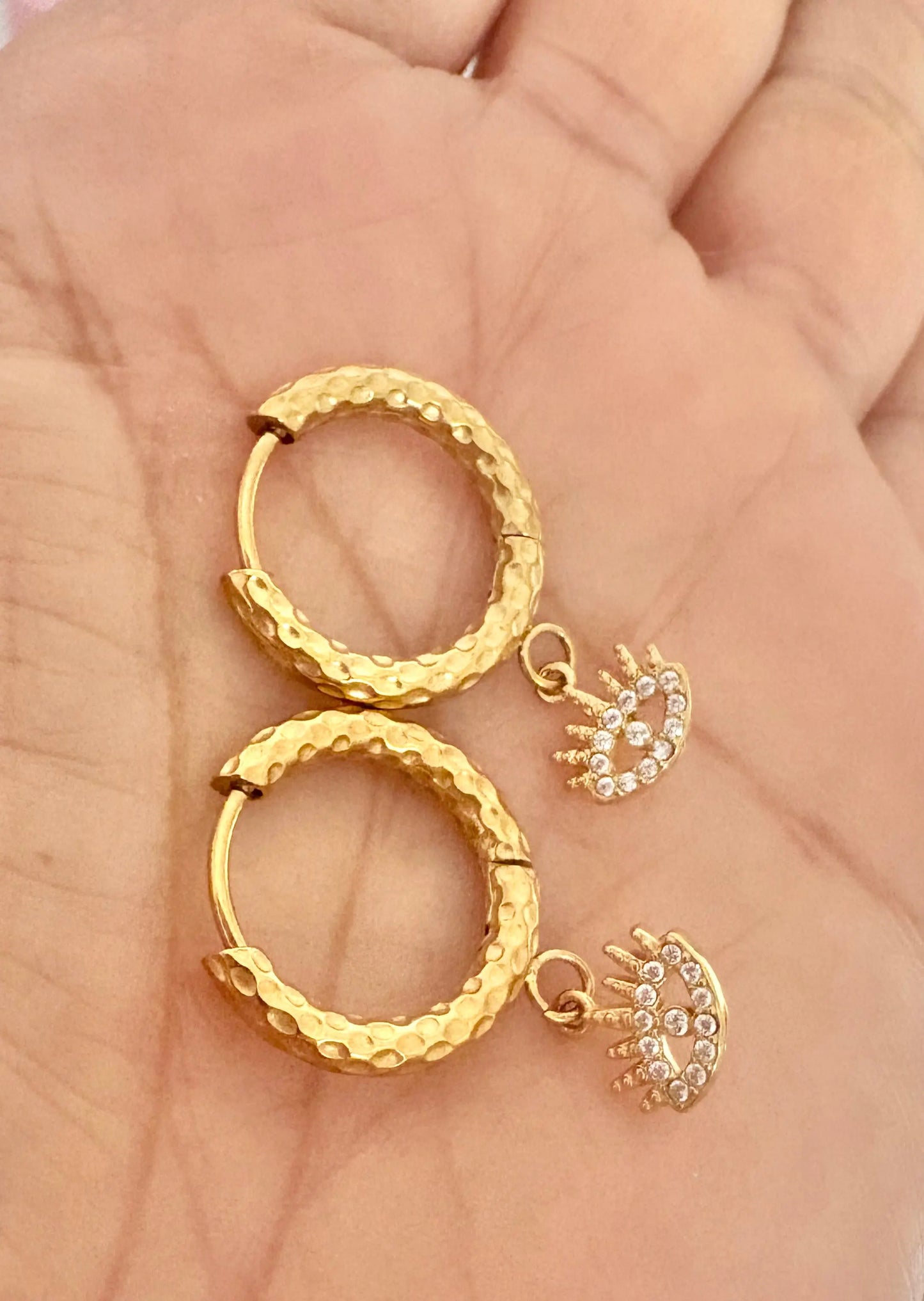 A pair of textured gold hoop earrings with small dangling crescent-shaped charms 