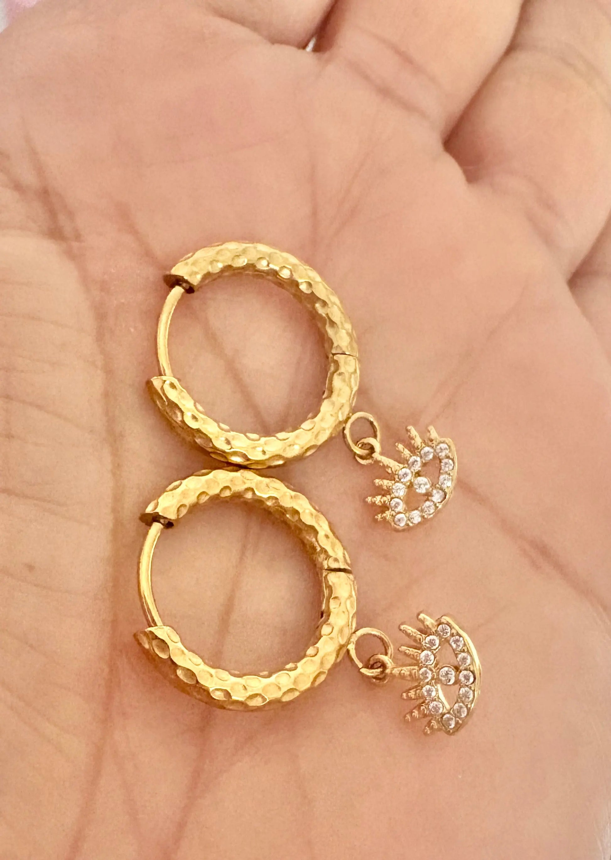 A pair of textured gold hoop earrings with small dangling crescent-shaped charms 
