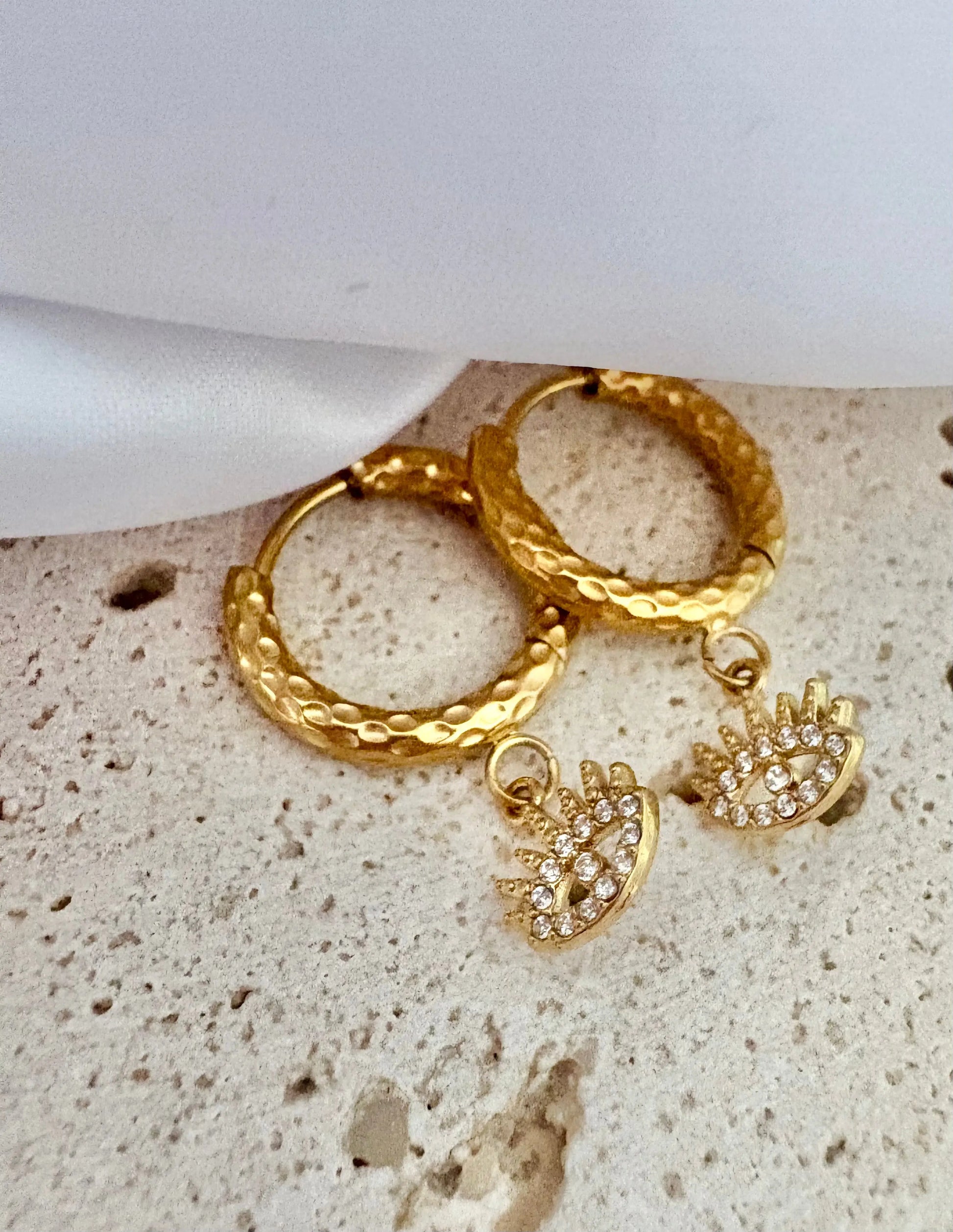 A pair of textured gold hoop earrings with dangling crown charms embellished with small clear zircon