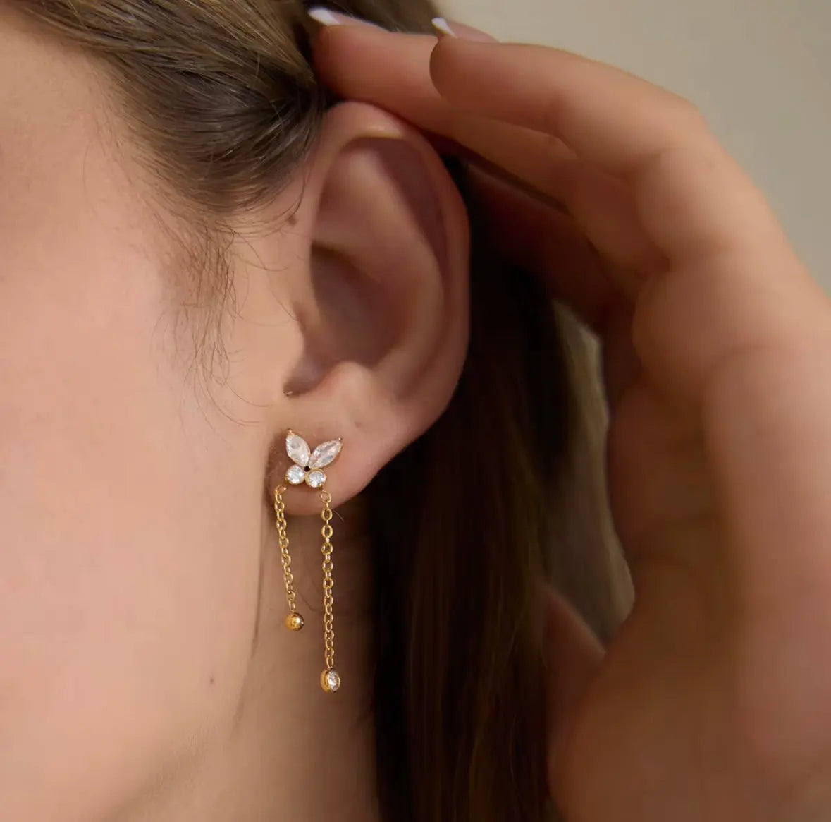 Close-up of a person wearing a delicate gold earring with a small butterfly design.