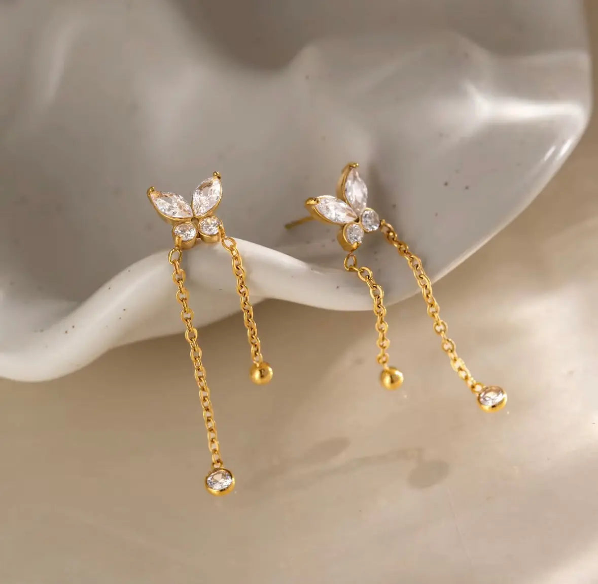 A pair of gold butterfly drop earrings with clear zircon-cut stones and dangling chain ends