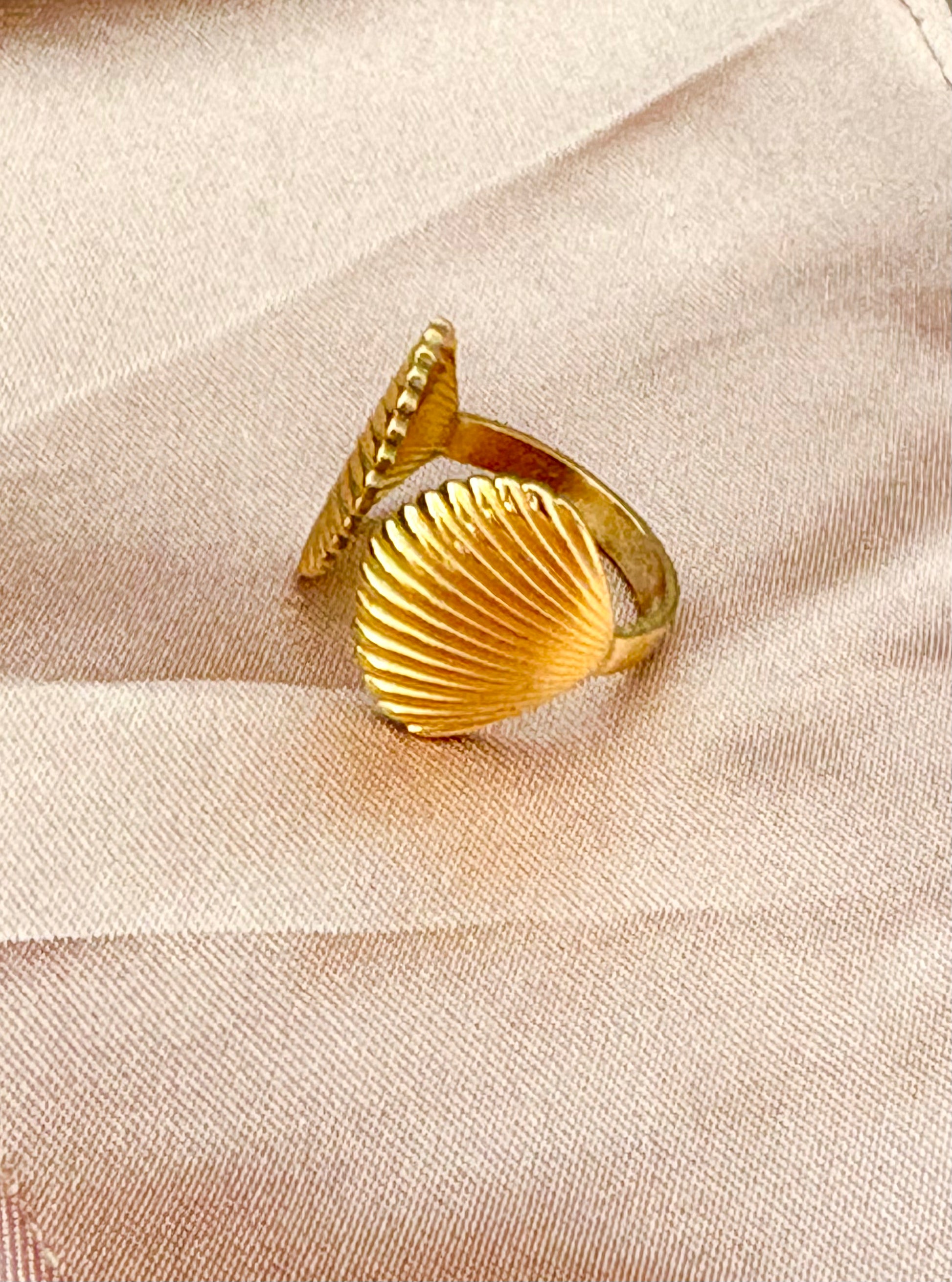 Gold shell-shaped ring on a beige fabric background