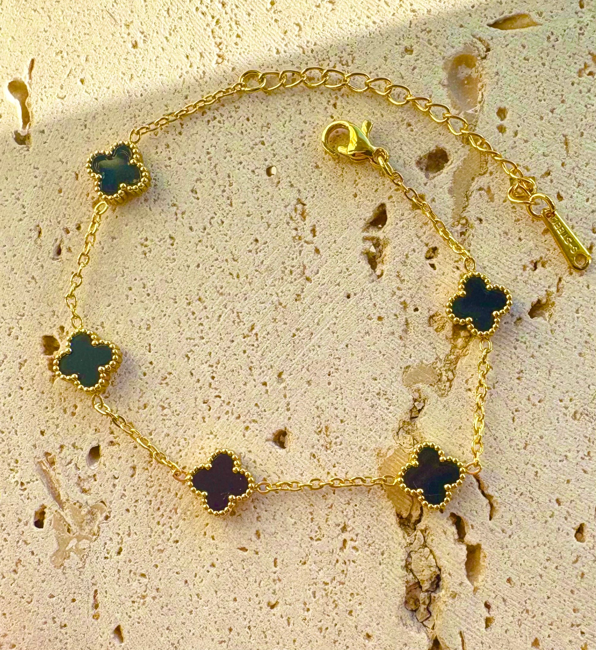 Gold bracelet with clover-shaped green stones on a textured beige surface