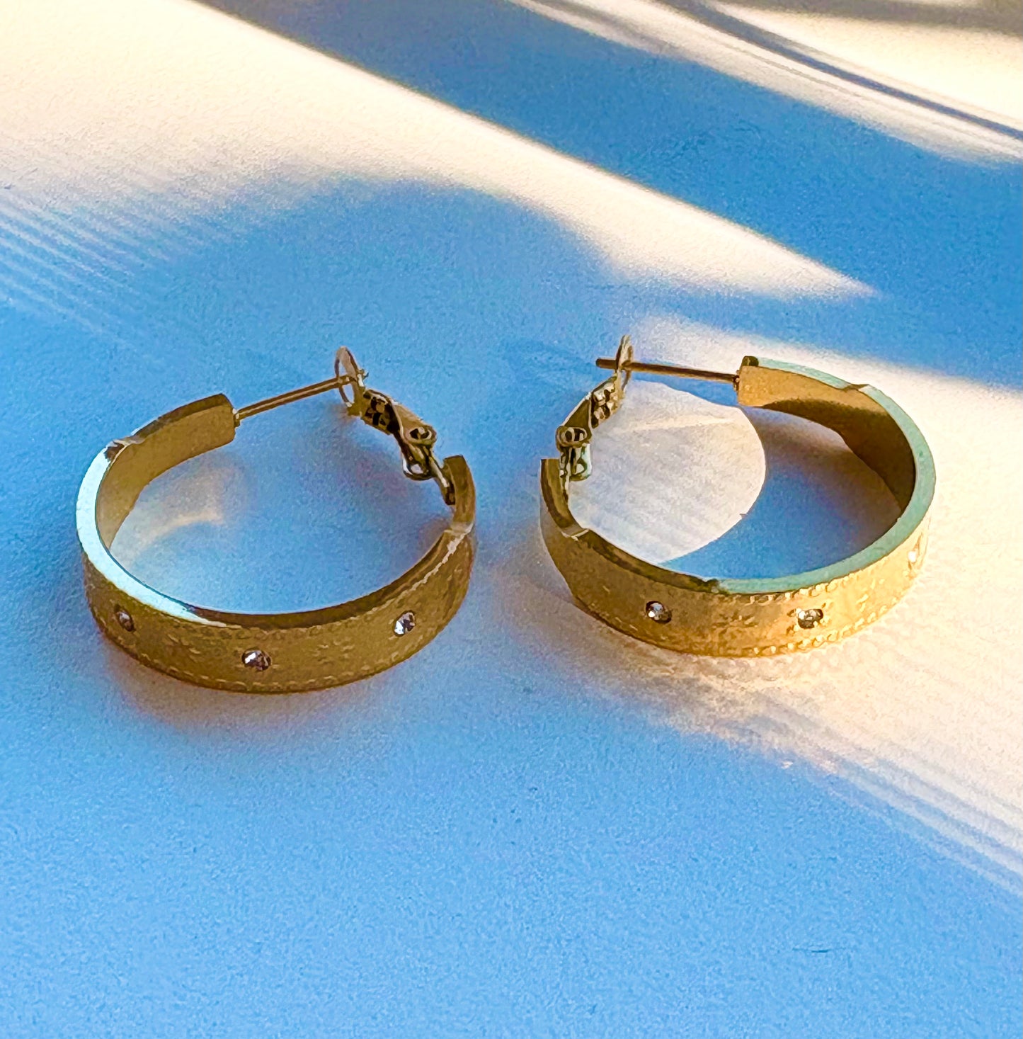 Close‑up of a gold hoop earring showing detailed star and dot engravings with crystal stones