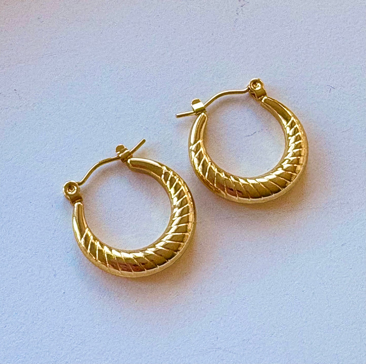 Pair of small gold hoop earrings featuring diagonal engravings and a polished finish