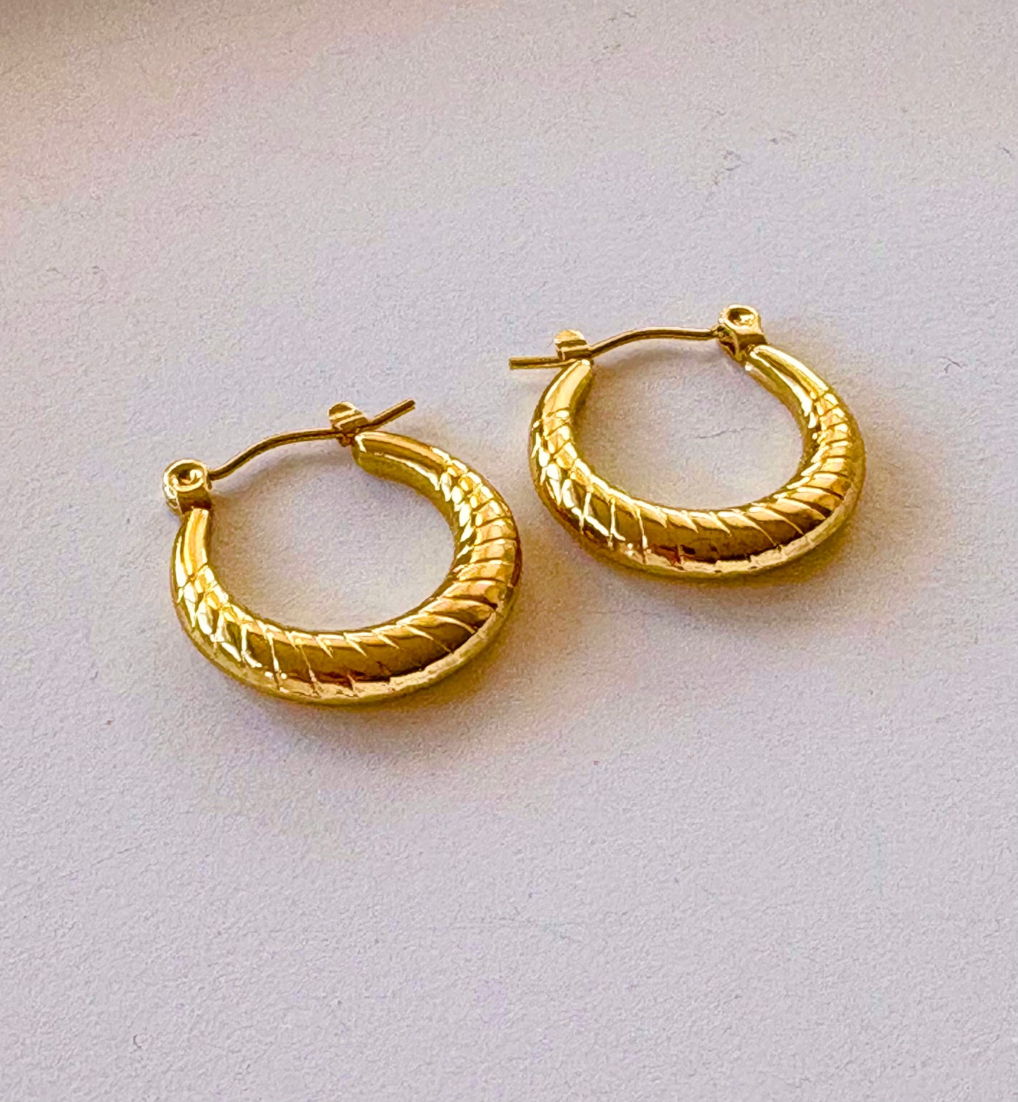 Close‑up of the twisted engraved pattern on a gold hoop earring showing 18k gold plating