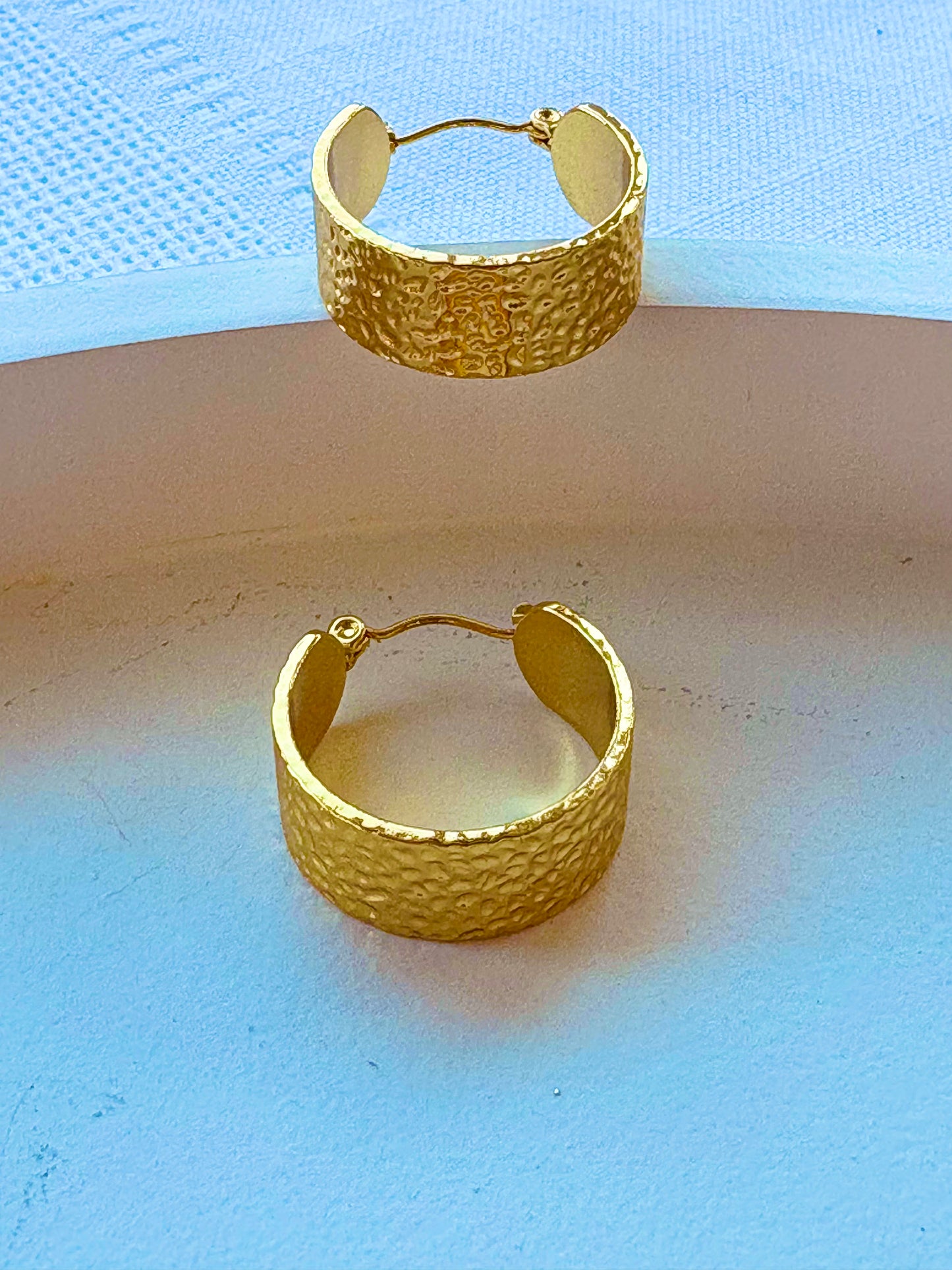 Gold hoop earrings on a textured surface with a light blue background