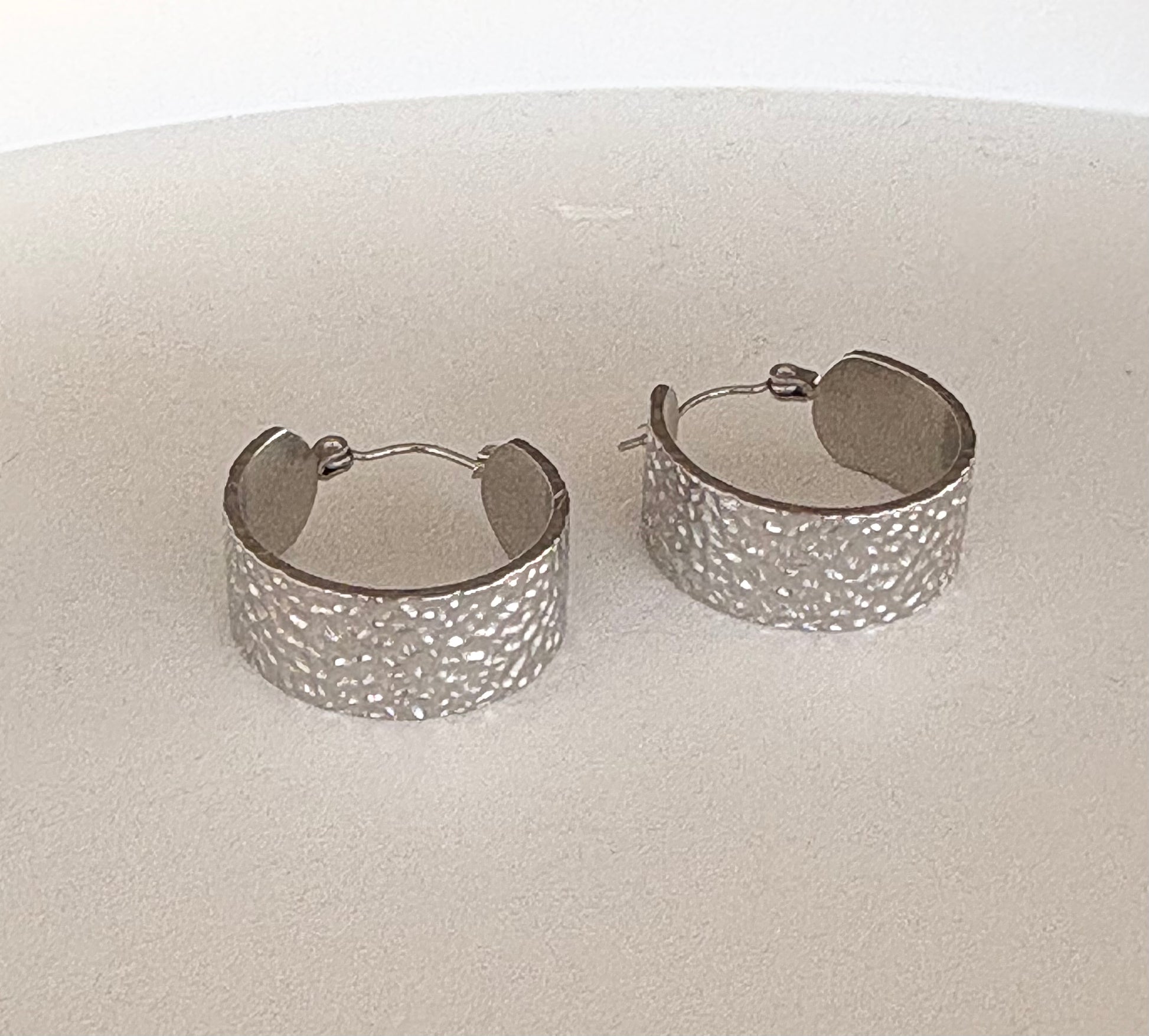 Pair of silver hoop earrings on a light beige surface