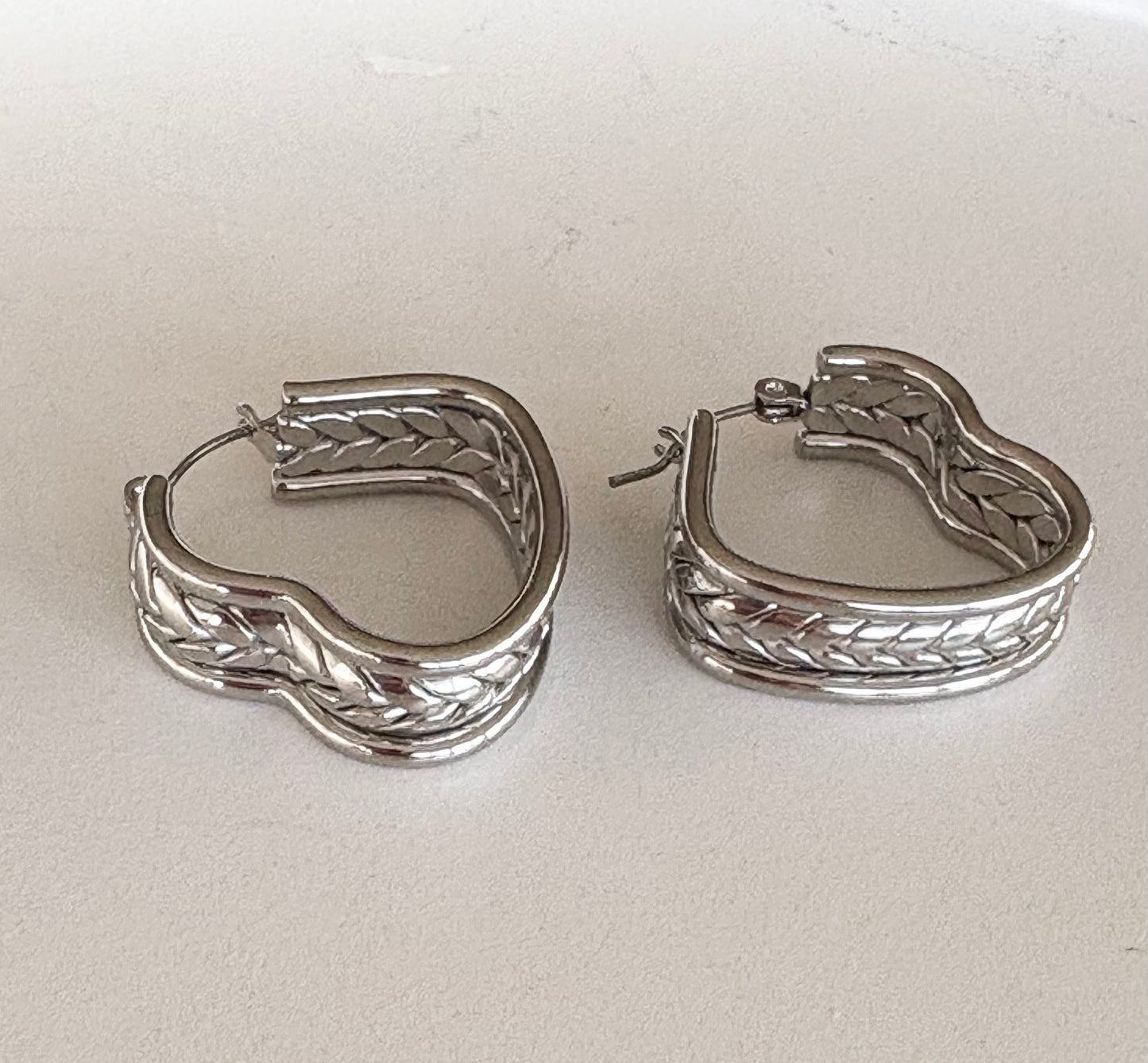 Close‑up of the braided texture on a silver heart hoop earring, highlighting its intricate weave