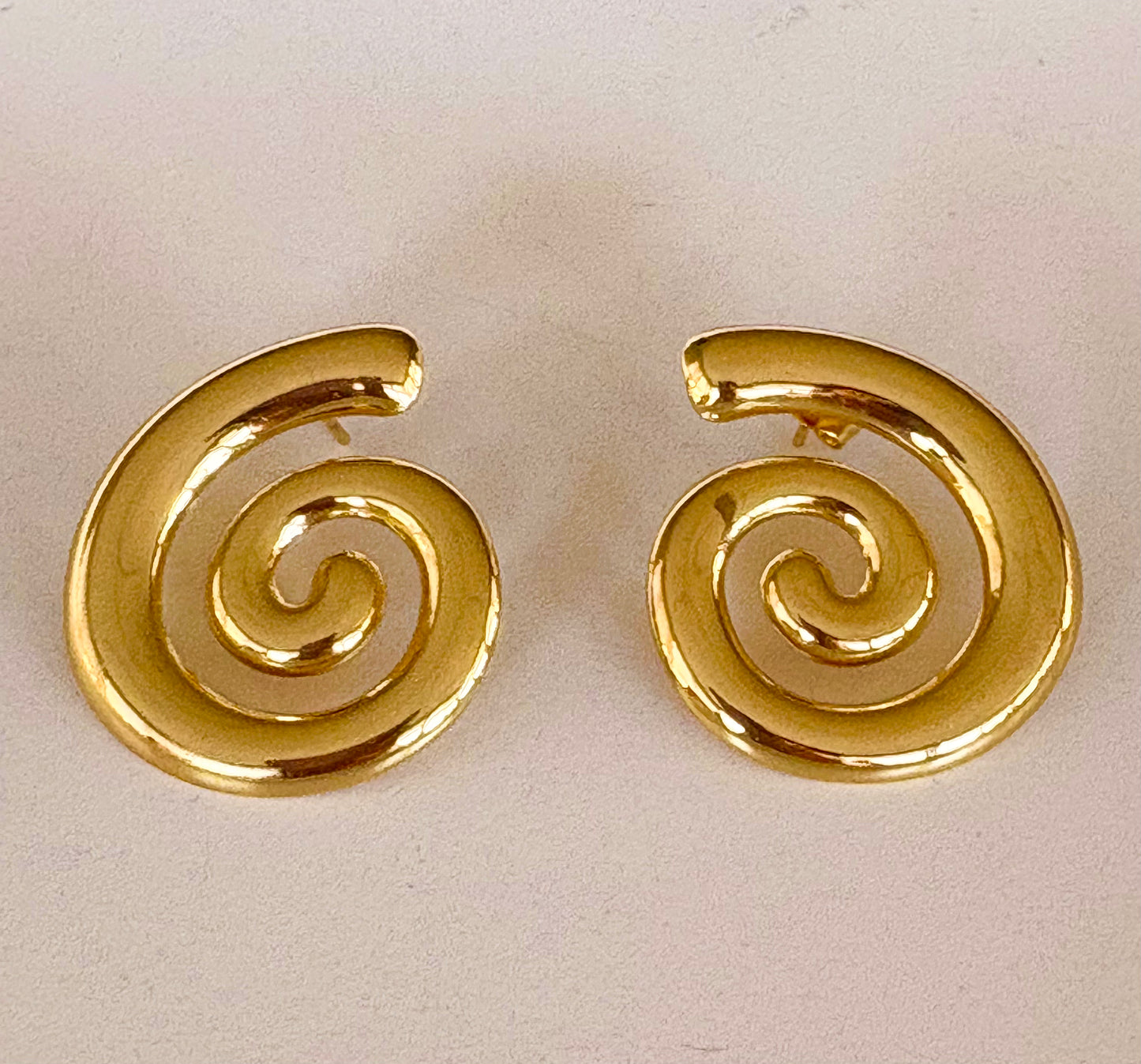 Pair of gold spiral earrings on a light beige background
