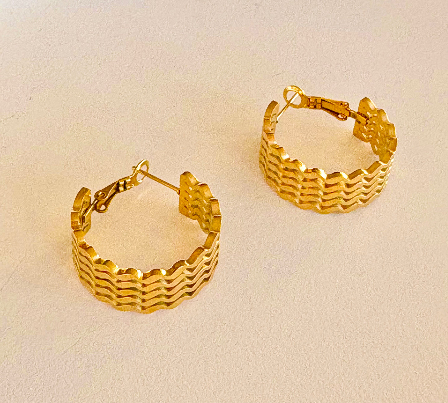 Close-up of the textured surface on a single gold hoop earring, highlighting the unique wave pattern.
