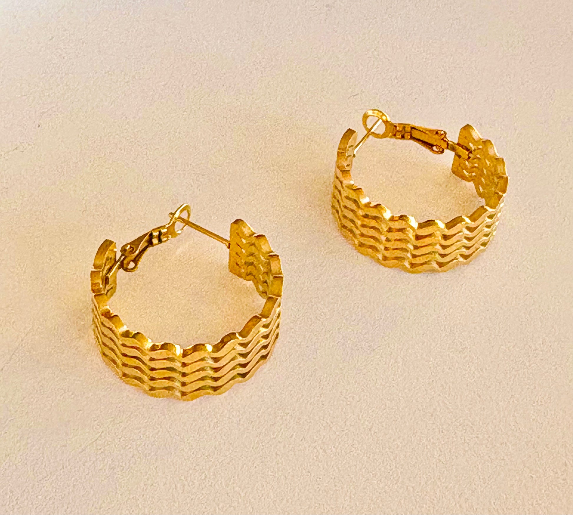 Close-up of the textured surface on a single gold hoop earring, highlighting the unique wave pattern.