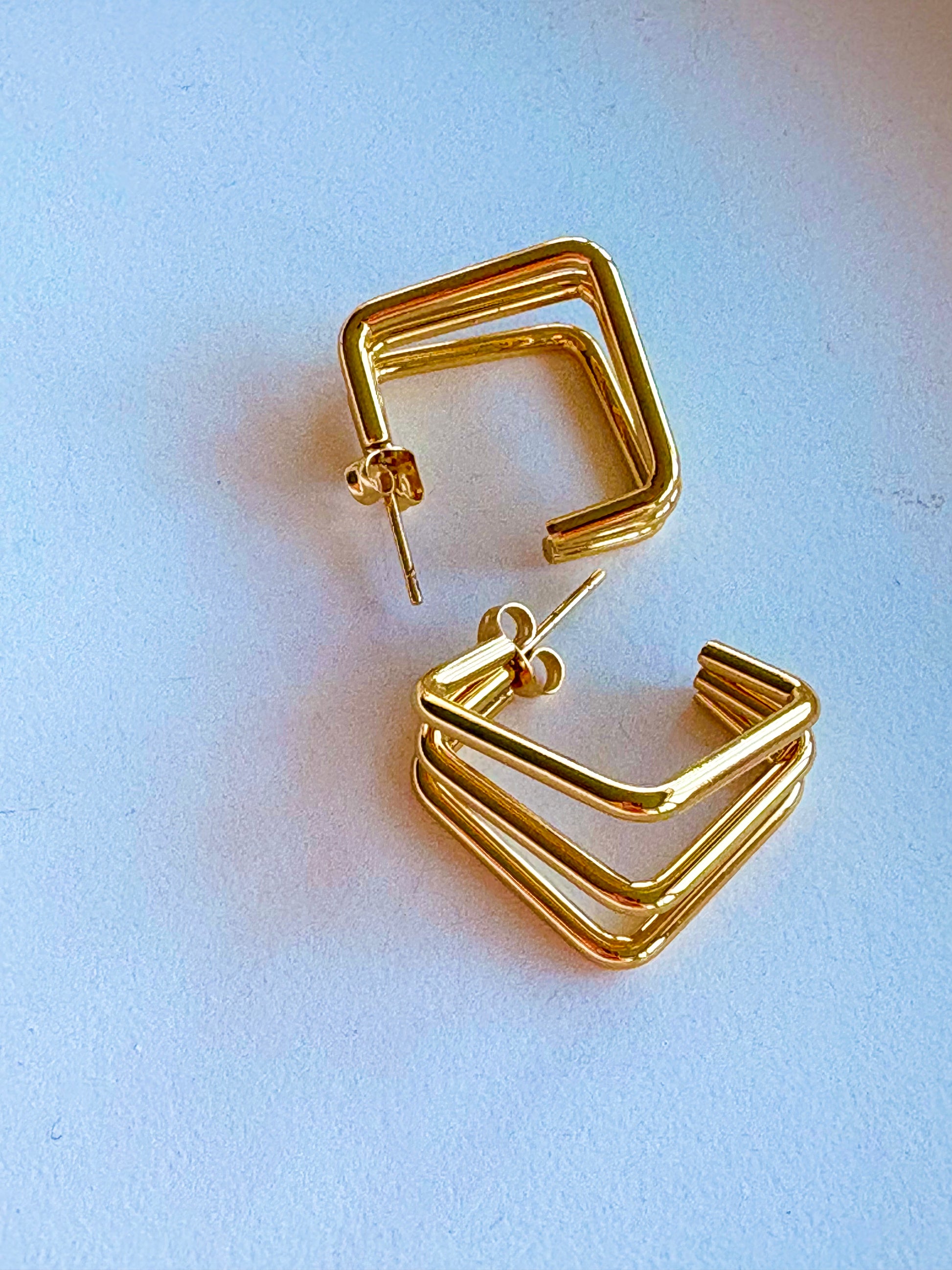 Front view of contemporary gold earrings featuring three stacked square hoops