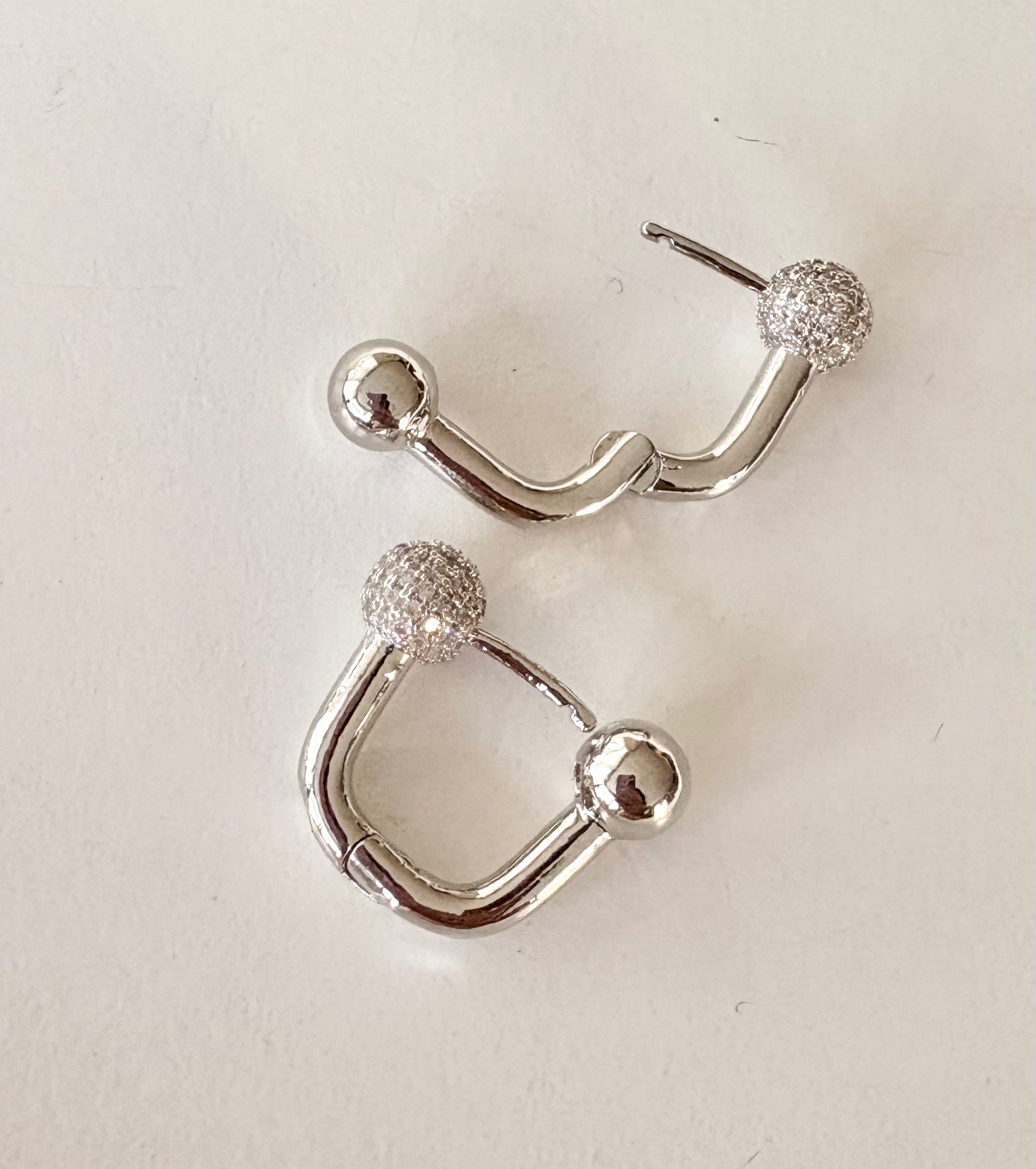 Close‑up of the textured ball on a U‑shaped hoop earring, highlighting the contrasting polished opposite sphere