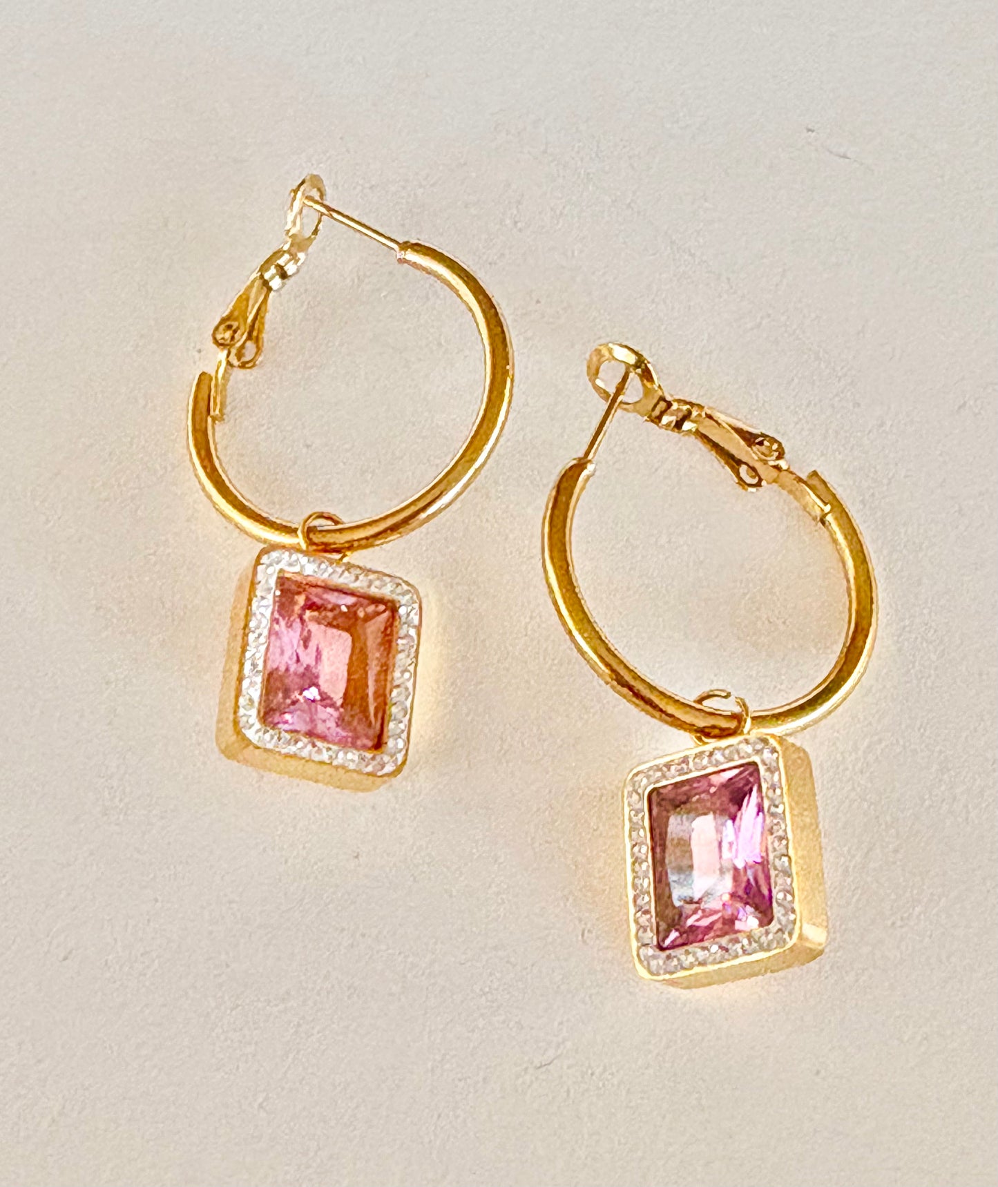 Close-up of gold hoop earrings with pink gemstone drop, elegant and waterproof jewelry design.