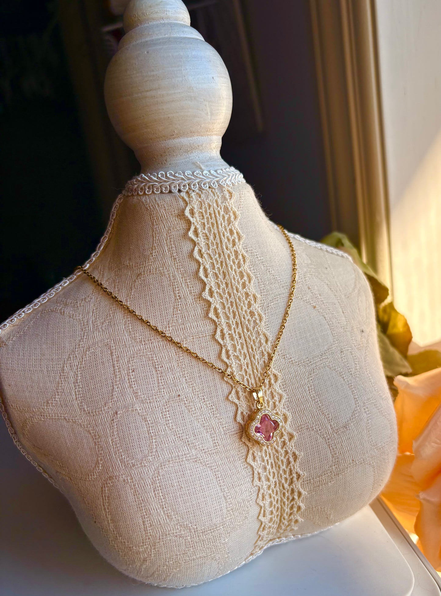 Necklace with a pink pendant on a lace-trimmed mannequin bust.