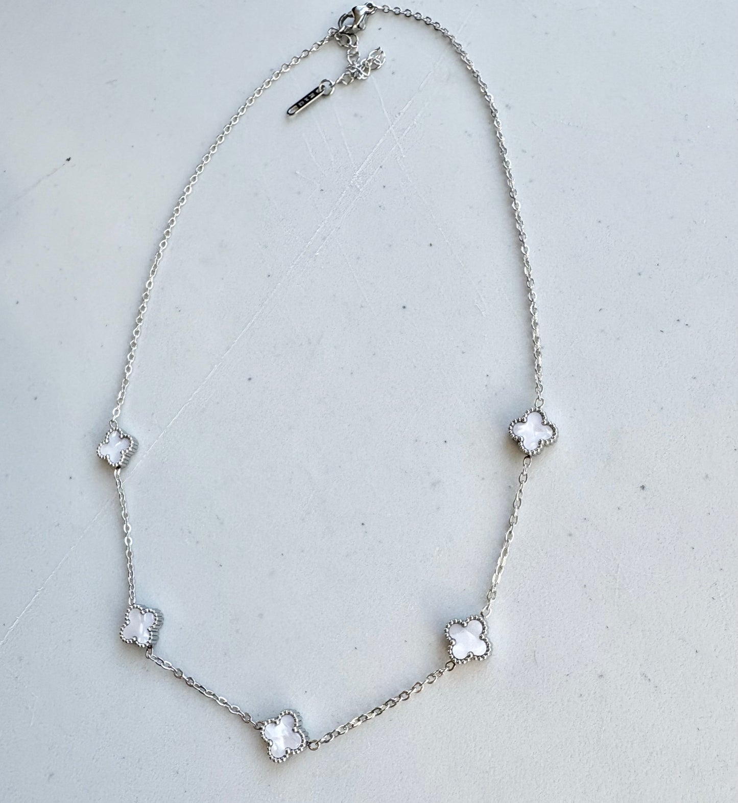 Silver necklace with flower-shaped pendants on a light gray background