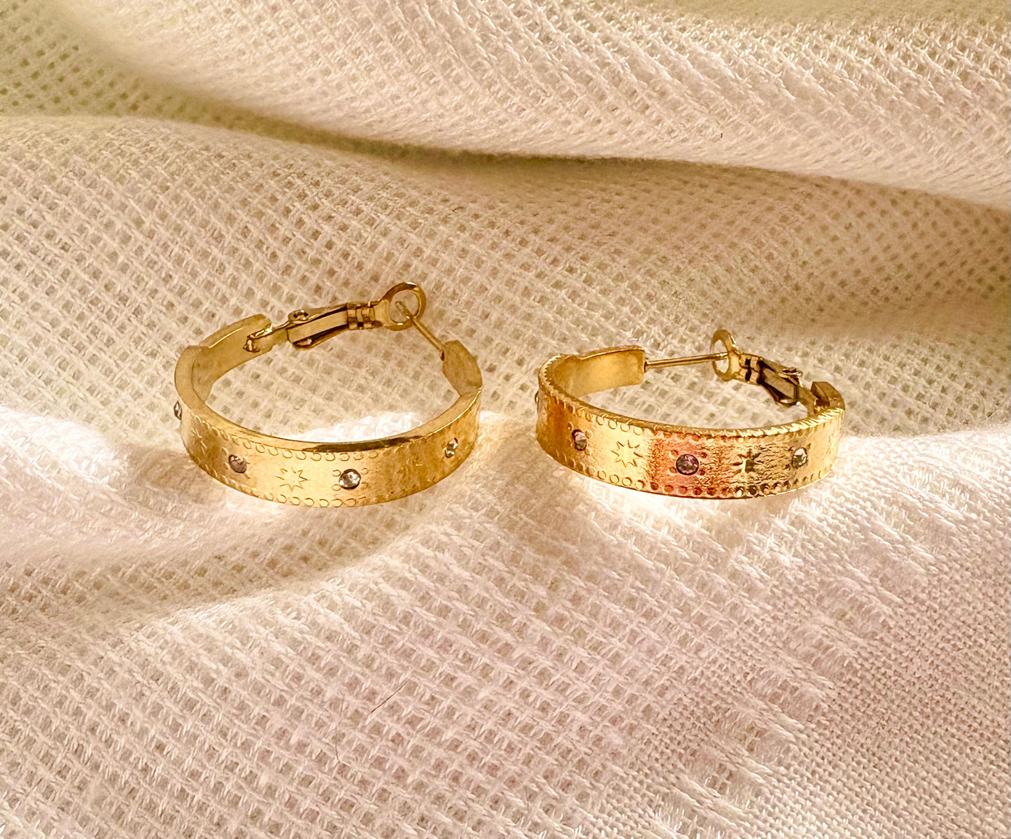 Engraved gold hoop earrings laid flat, highlighting the hammered texture, starburst pattern