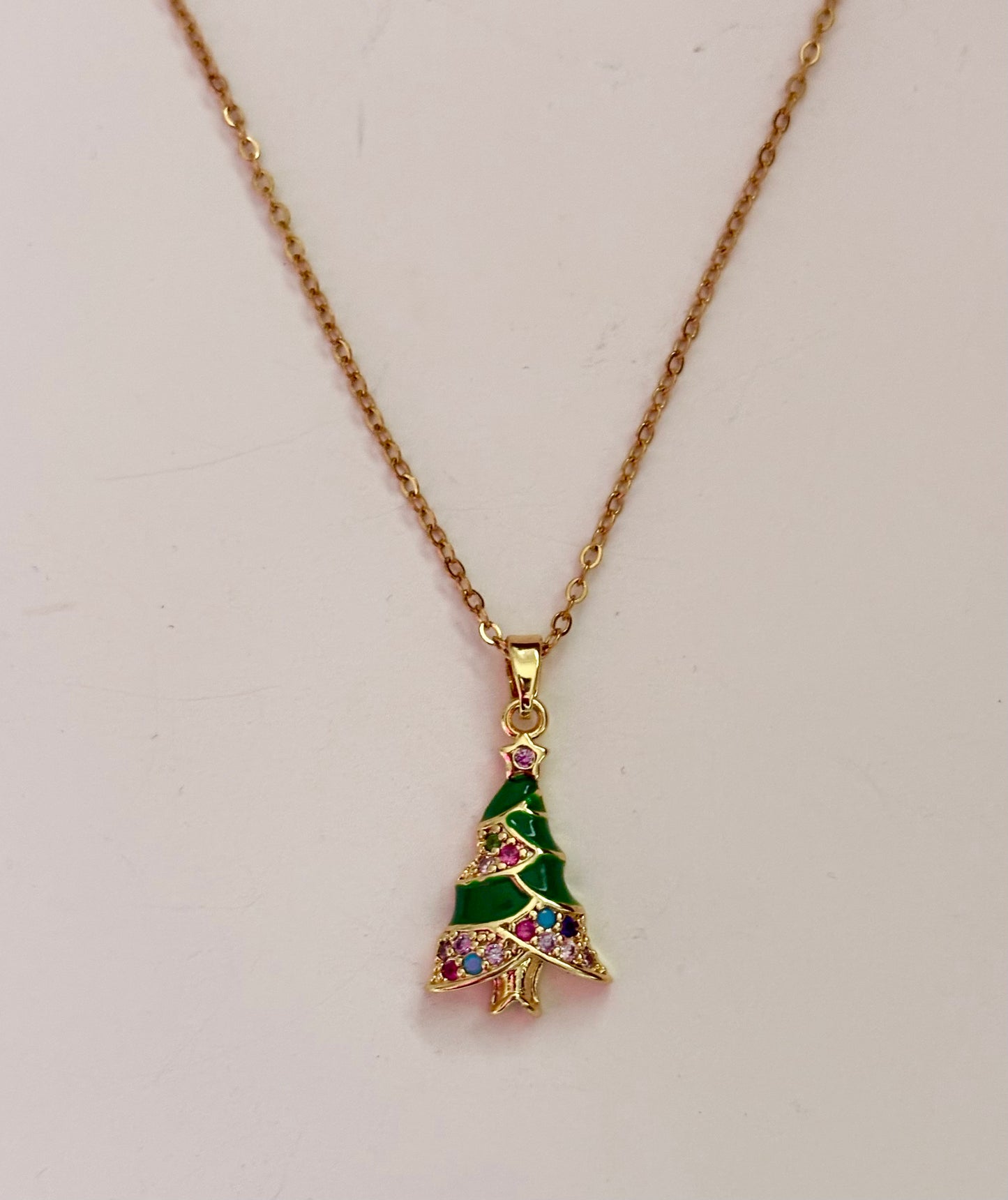Gold necklace with a green tree-shaped pendant on a light gray background
