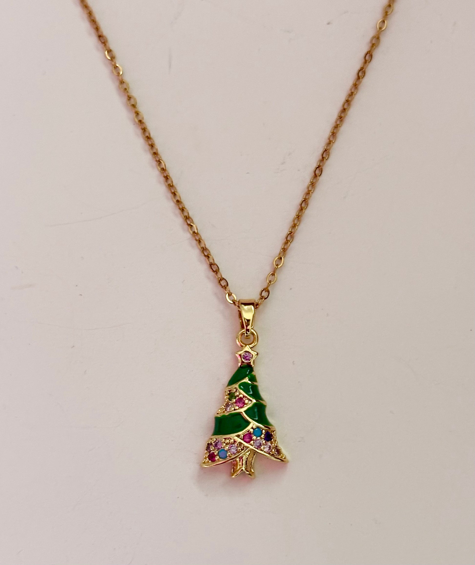 Gold necklace with a green tree-shaped pendant on a light gray background