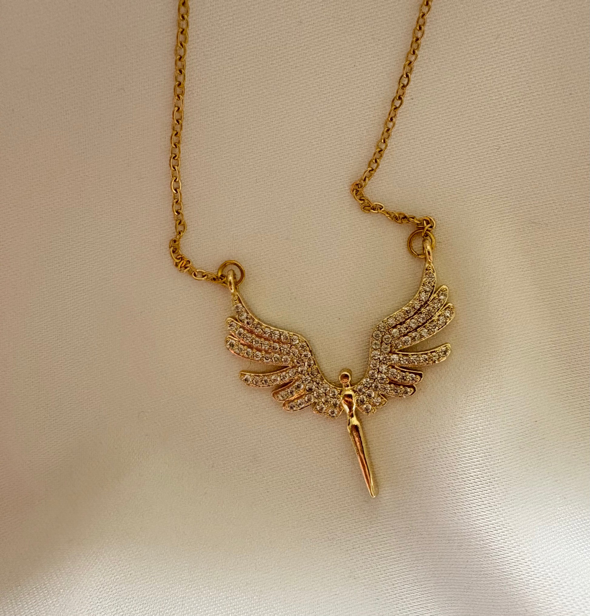 Gold necklace with a winged pendant on a beige background