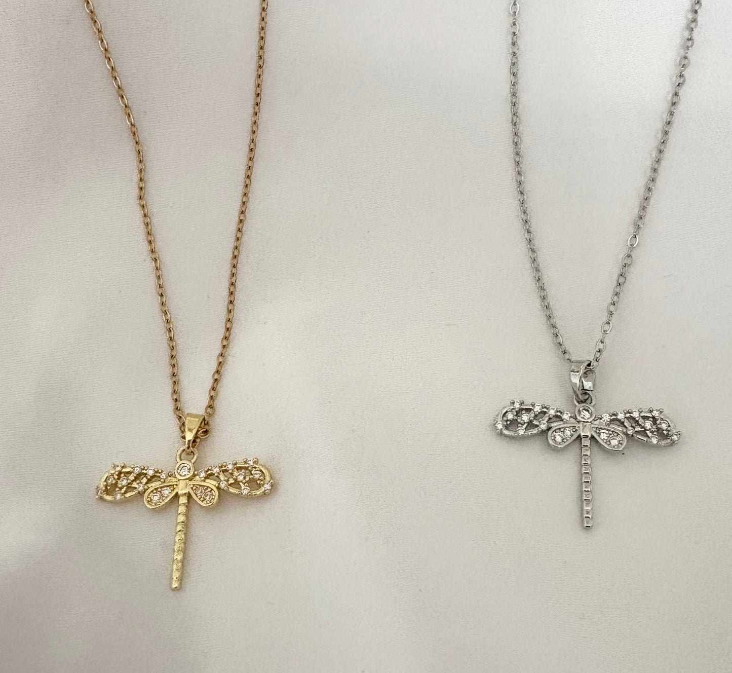 Two necklaces with dragonfly pendants, one gold and one silver, on a light gray background.