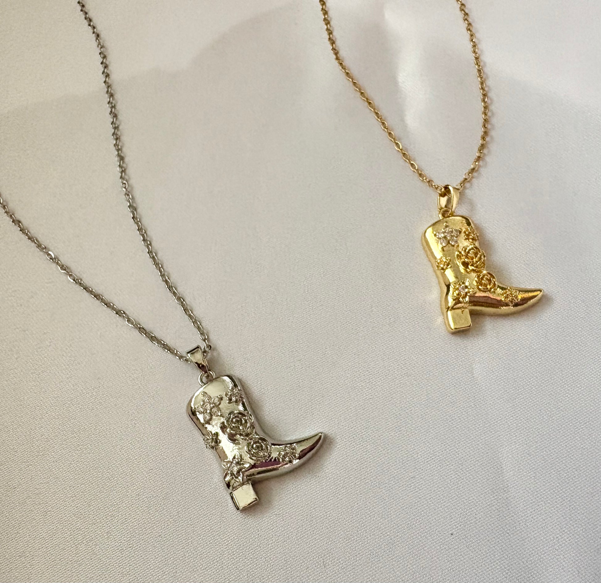 Side-by-side gold and silver Western boot necklaces on white background