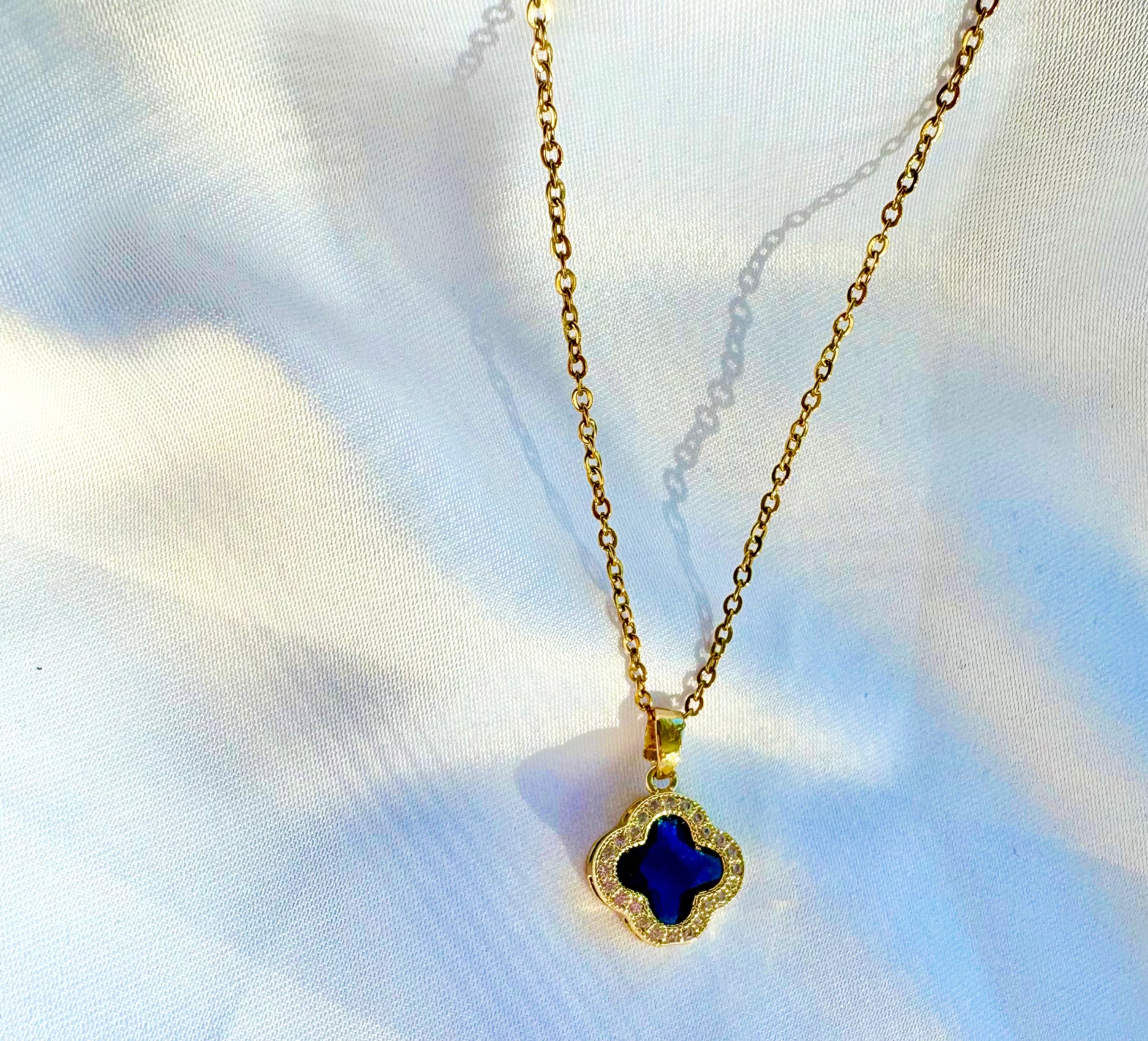 Gold necklace with a blue pendant on a white fabric background