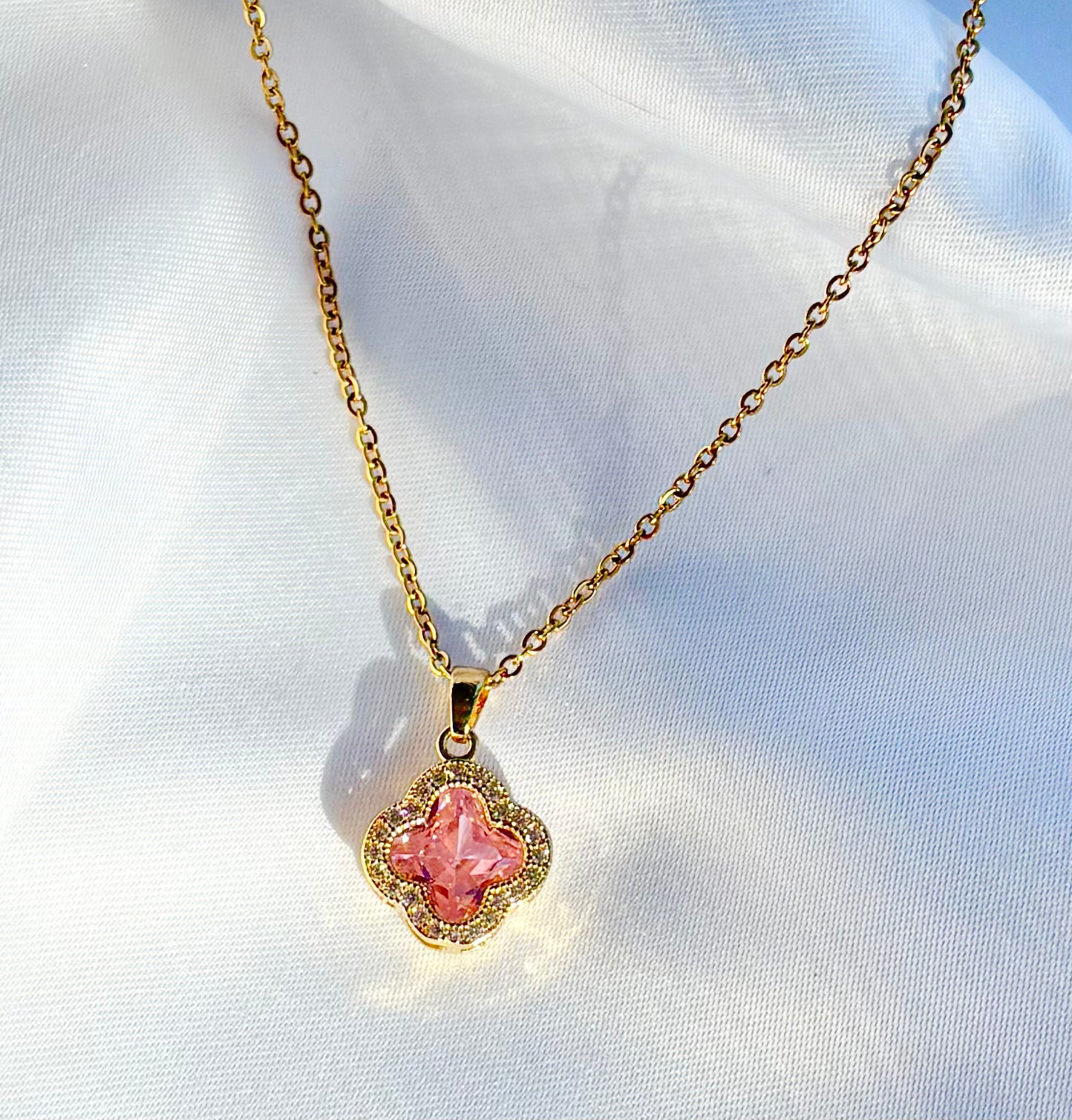 Gold necklace with a pink pendant on a white fabric background