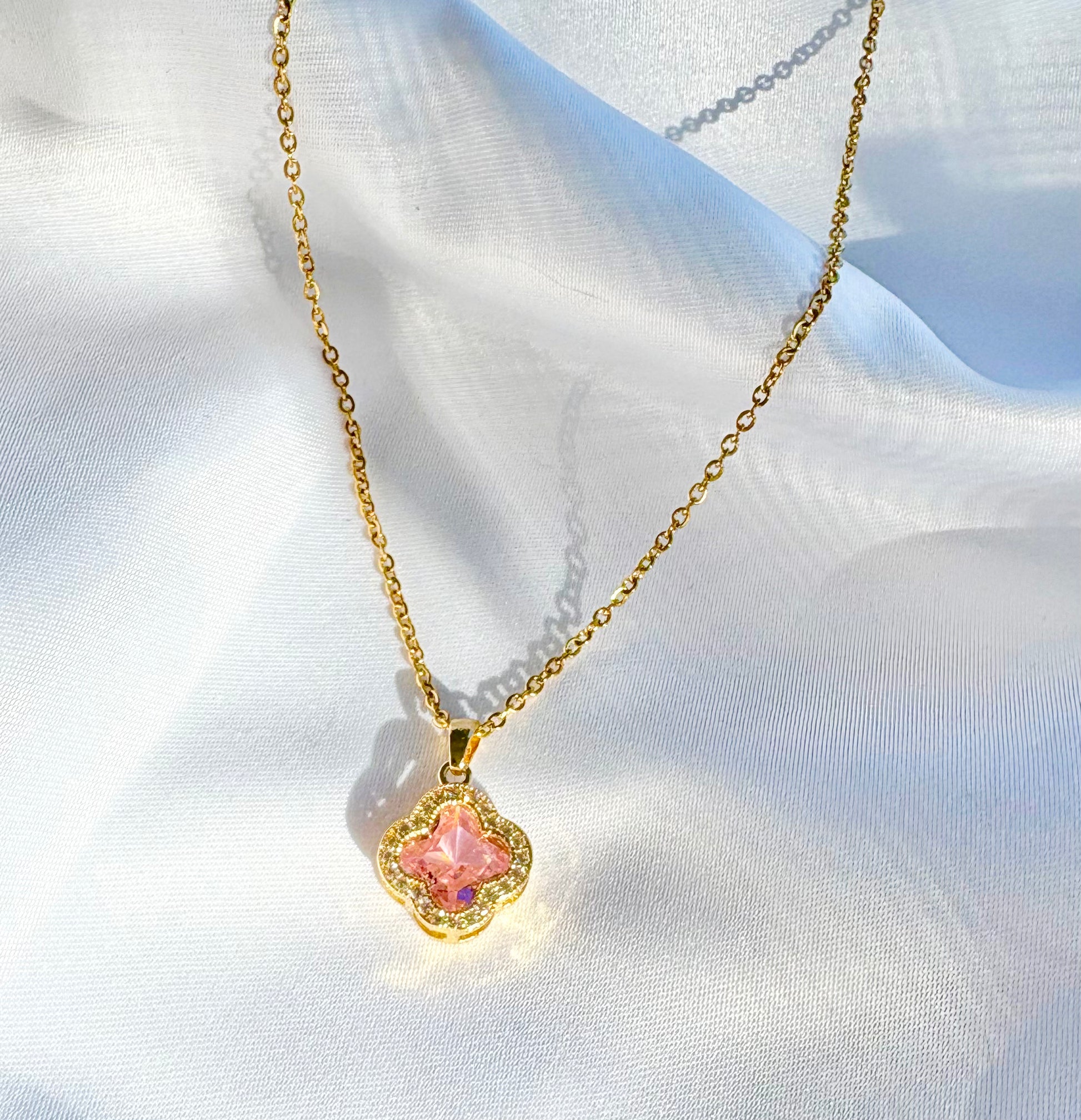 Gold necklace with a pink pendant on a white fabric background