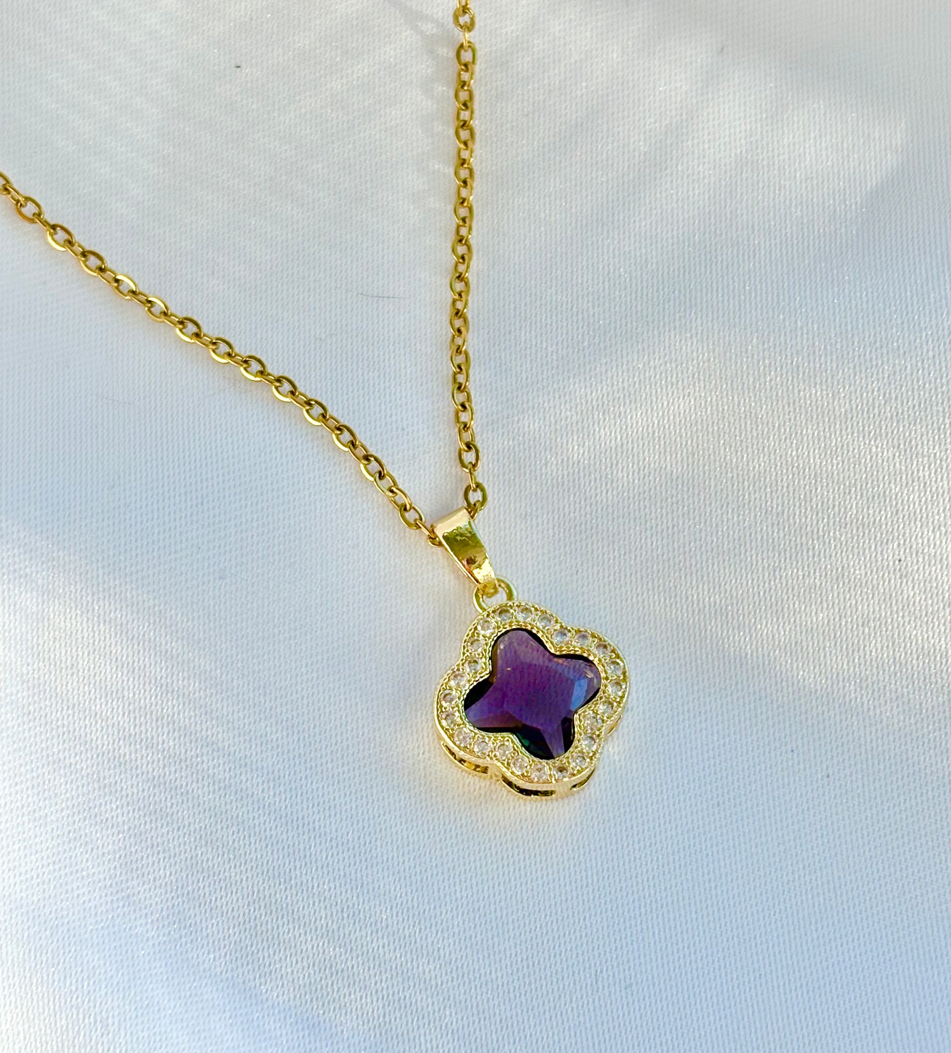 Gold necklace with a purple clover-shaped pendant on a white background