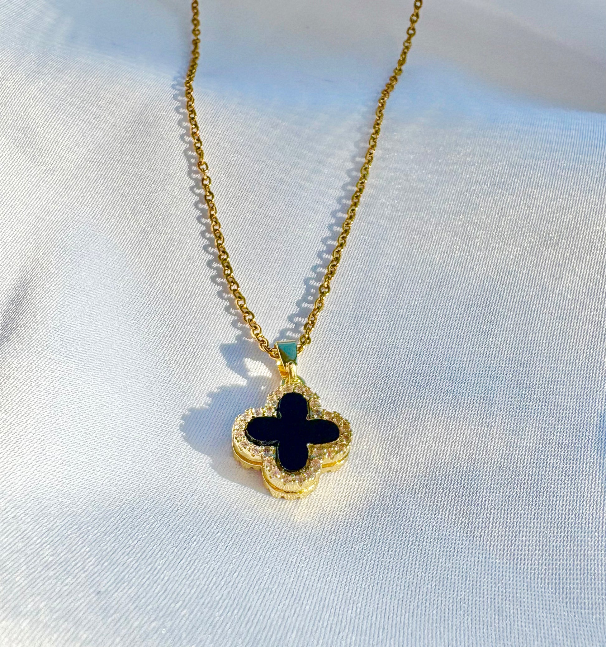 Gold necklace with a black clover pendant on a white background