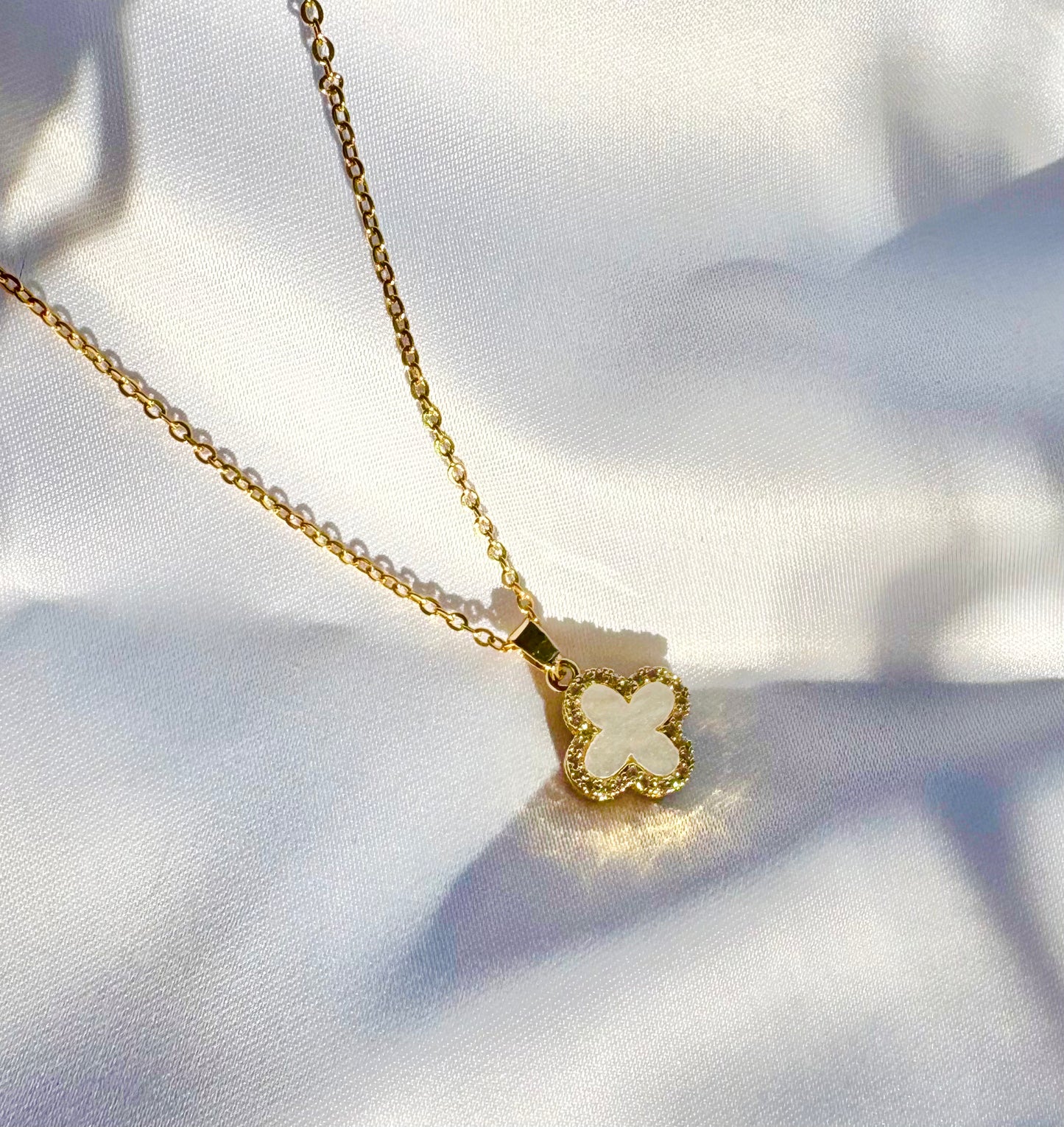 Gold necklace with a clover-shaped pendant on a white fabric background
