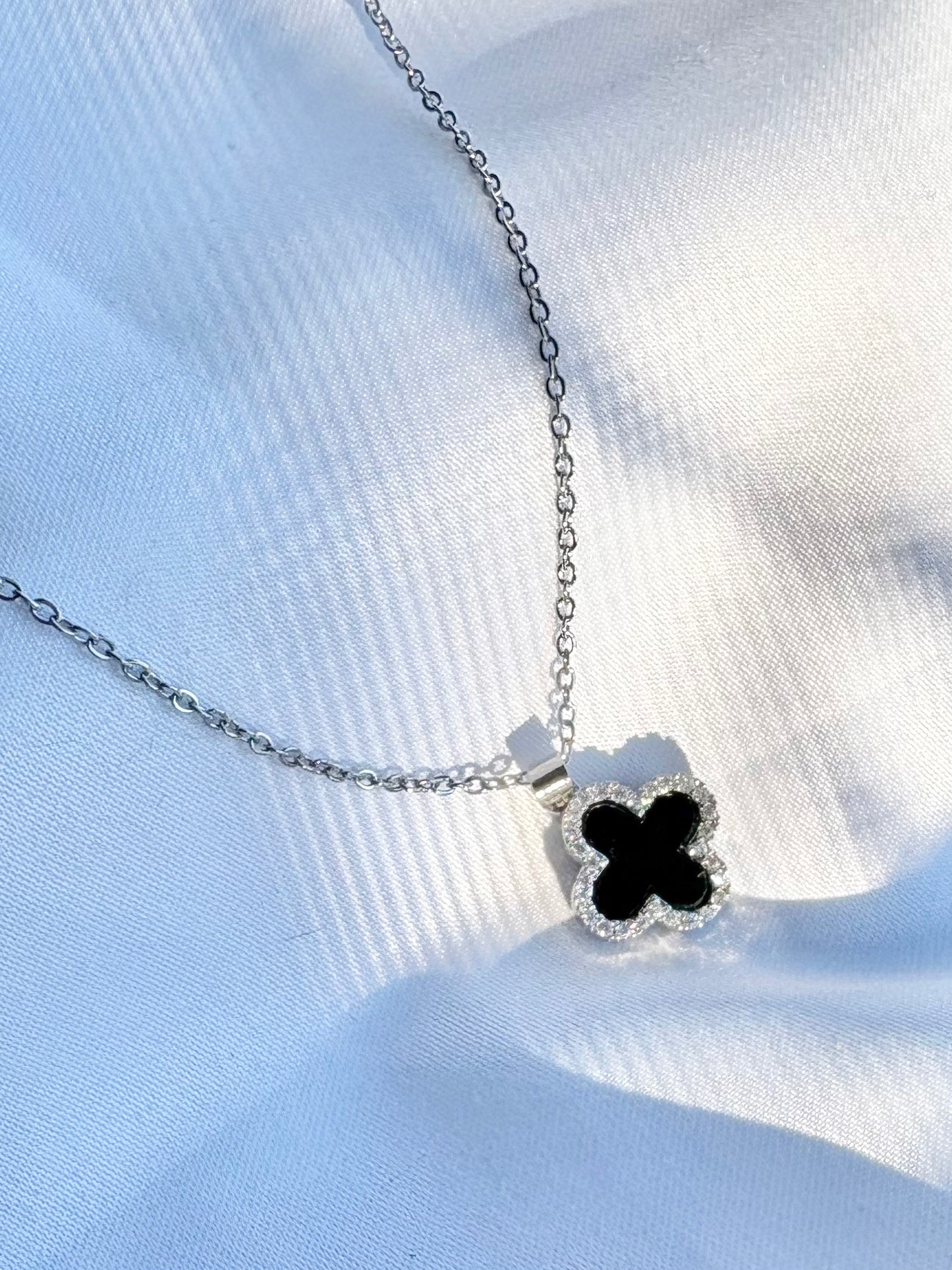 Elegant non-tarnish black clover pendant necklace displayed on fabric