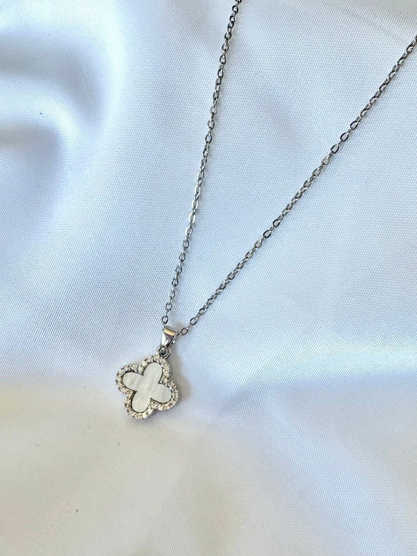 White clover pendant necklace on stainless steel chain displayed on white fabric.