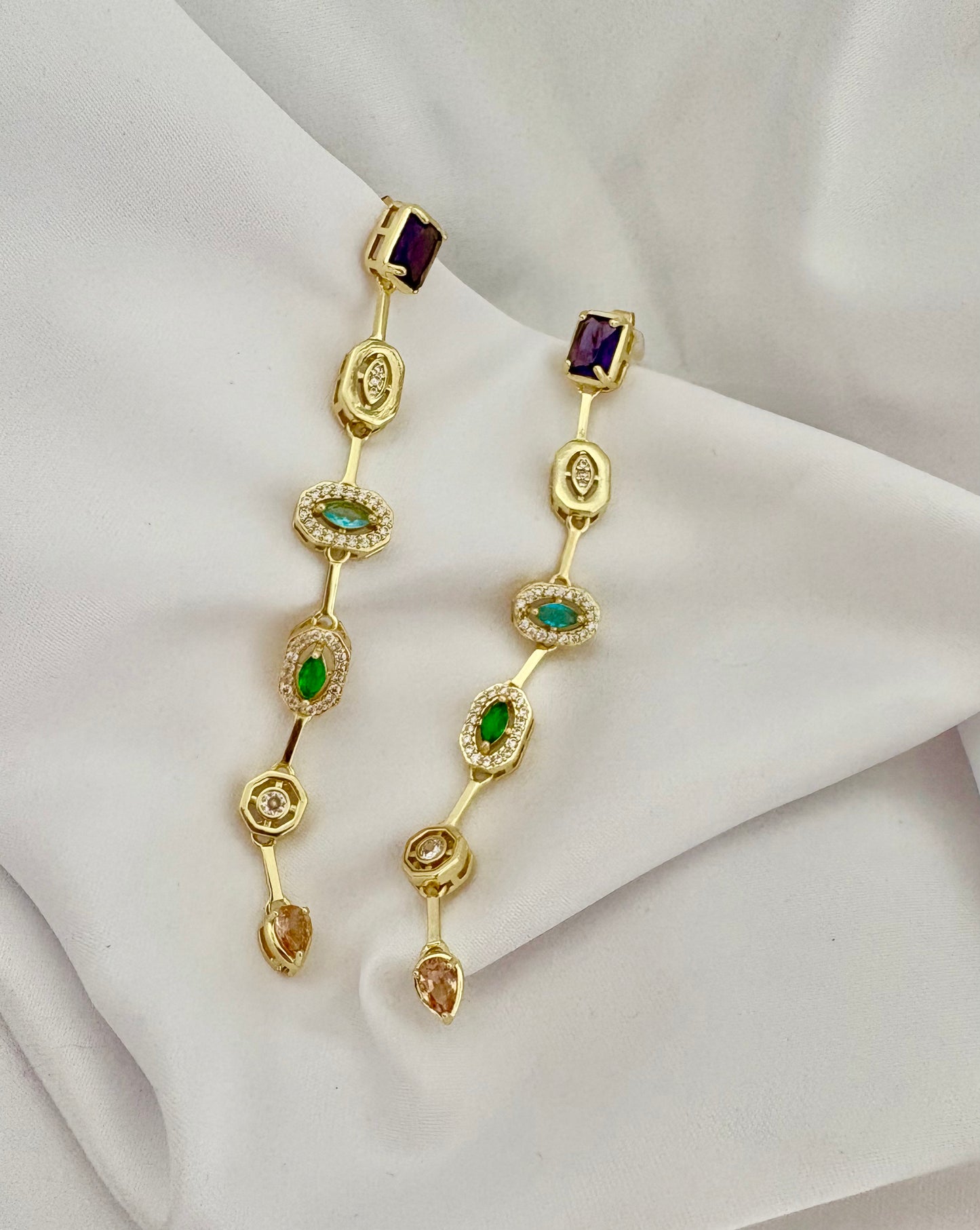 Gold earrings with gemstones on a white fabric background
