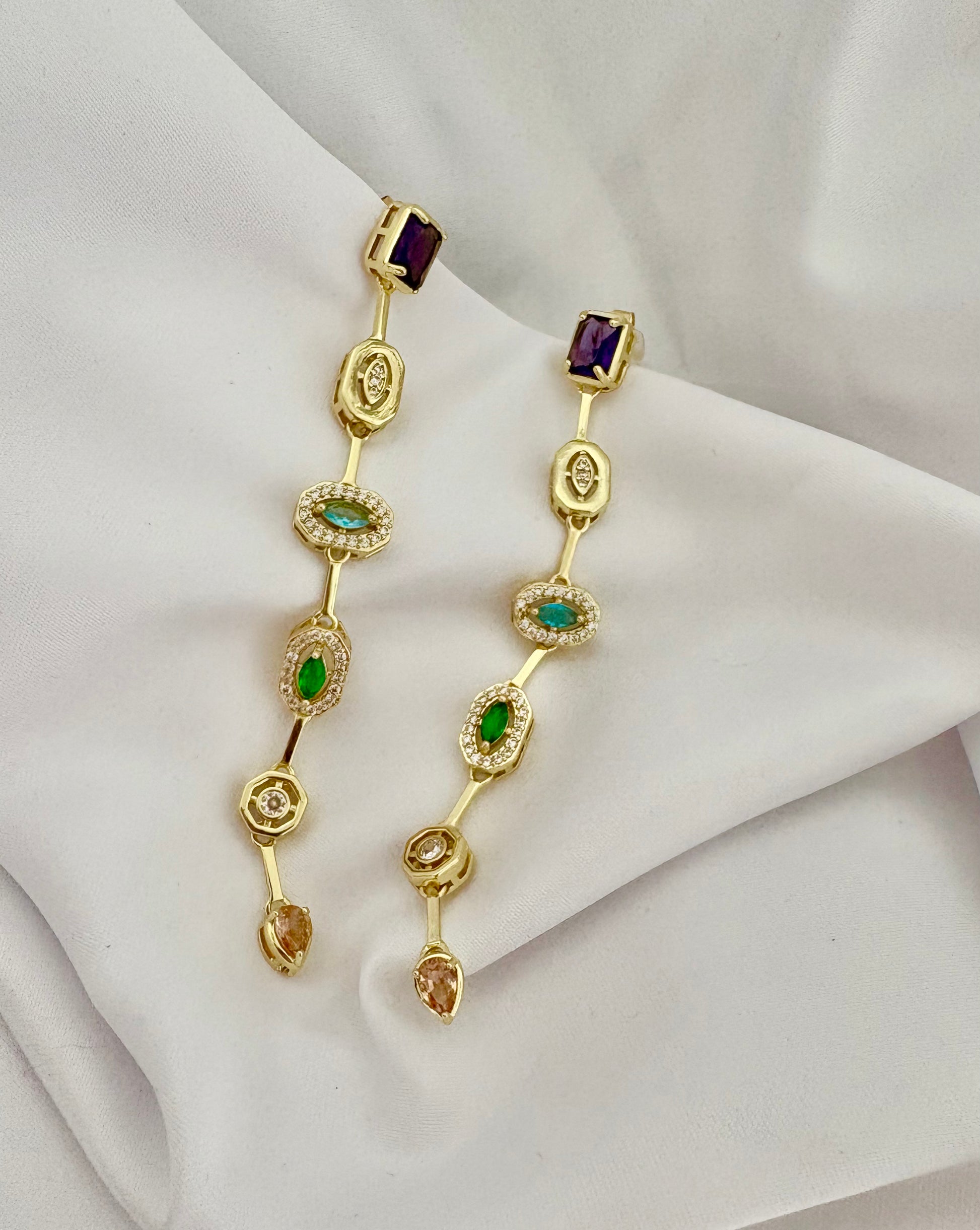 Gold earrings with gemstones on a white fabric background
