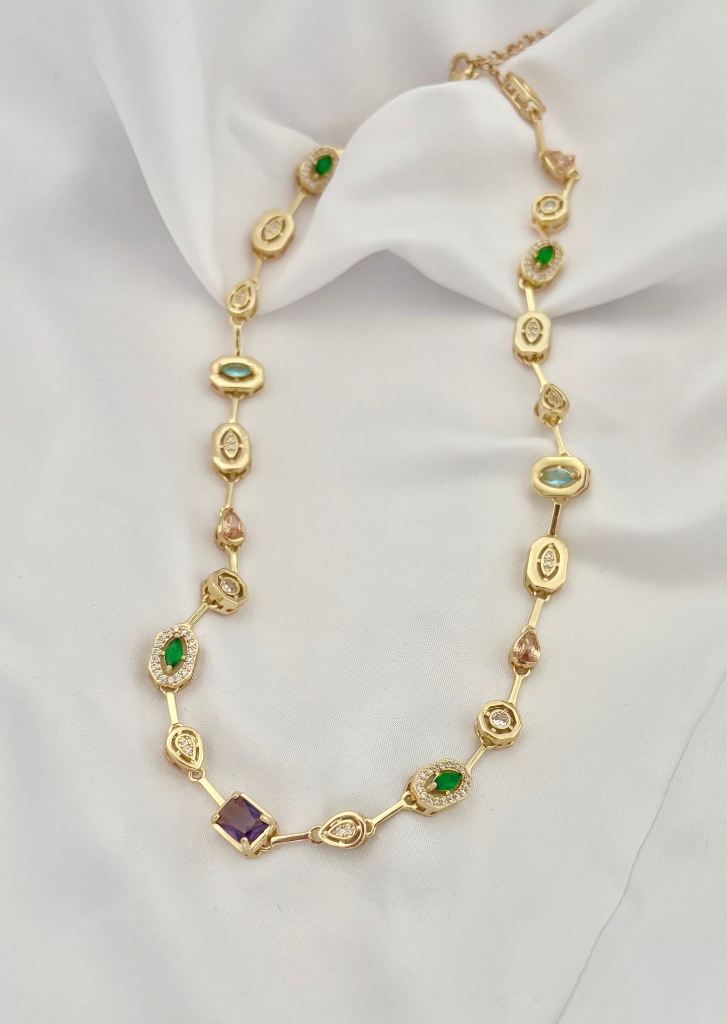 Gold necklace with gemstones on a white fabric background
