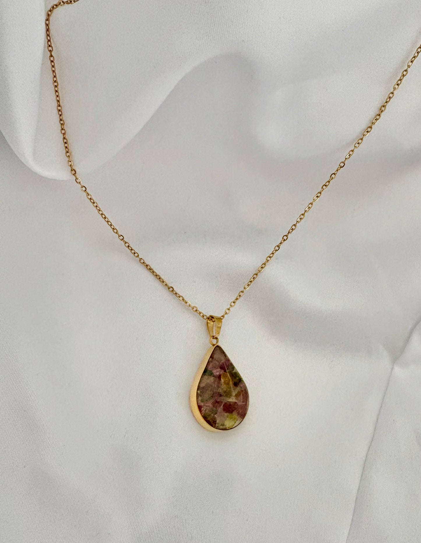 Gold necklace with a teardrop-shaped pendant on a white fabric background