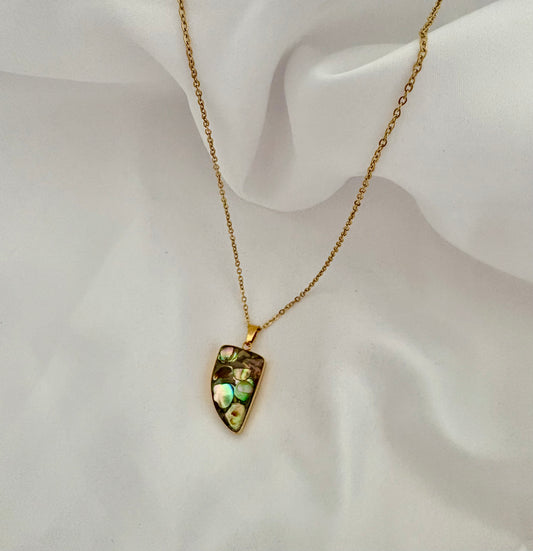 Gold necklace with a green gemstone pendant on a white fabric background