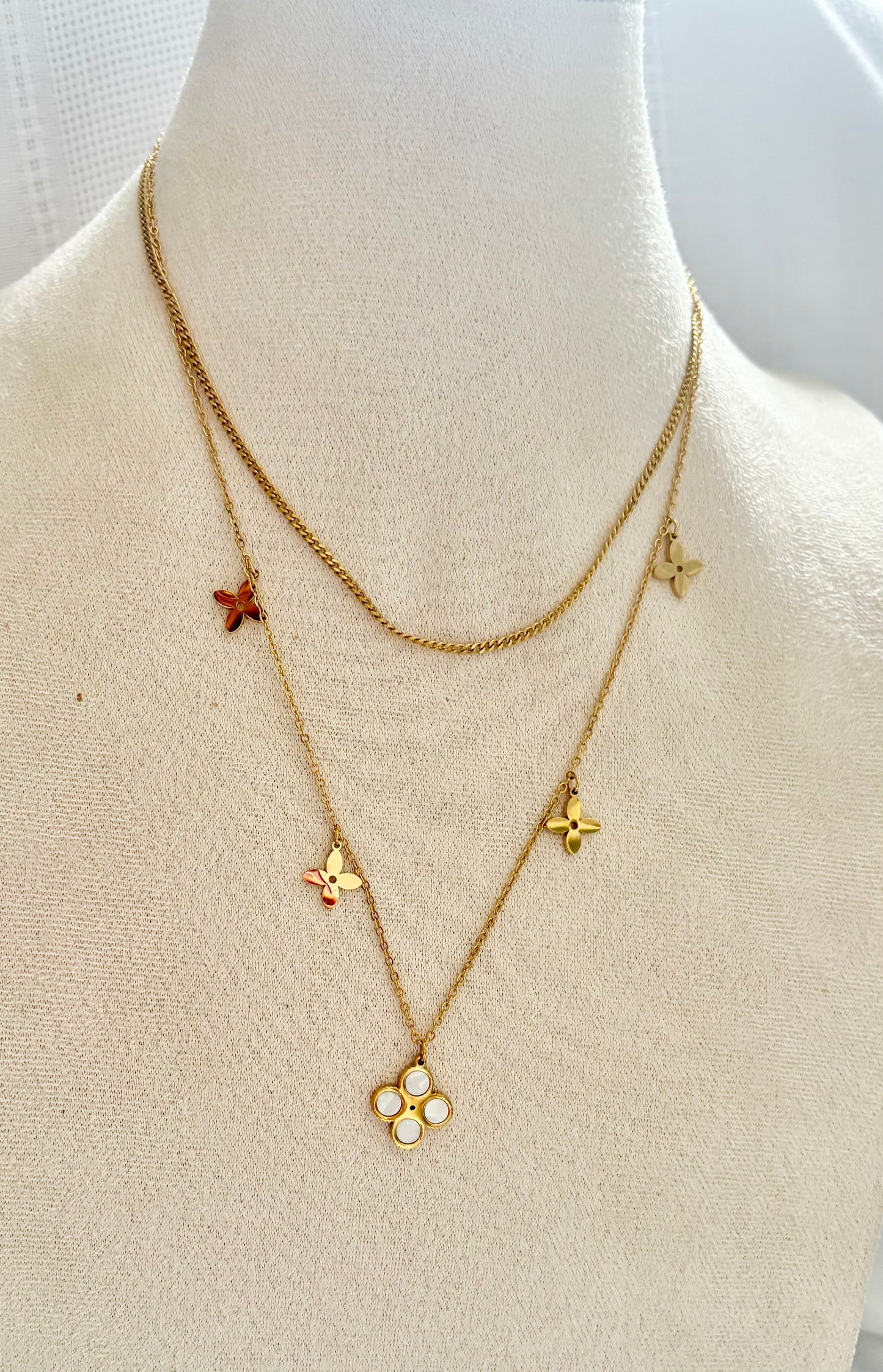 Gold necklaces with floral charms on a mannequin.