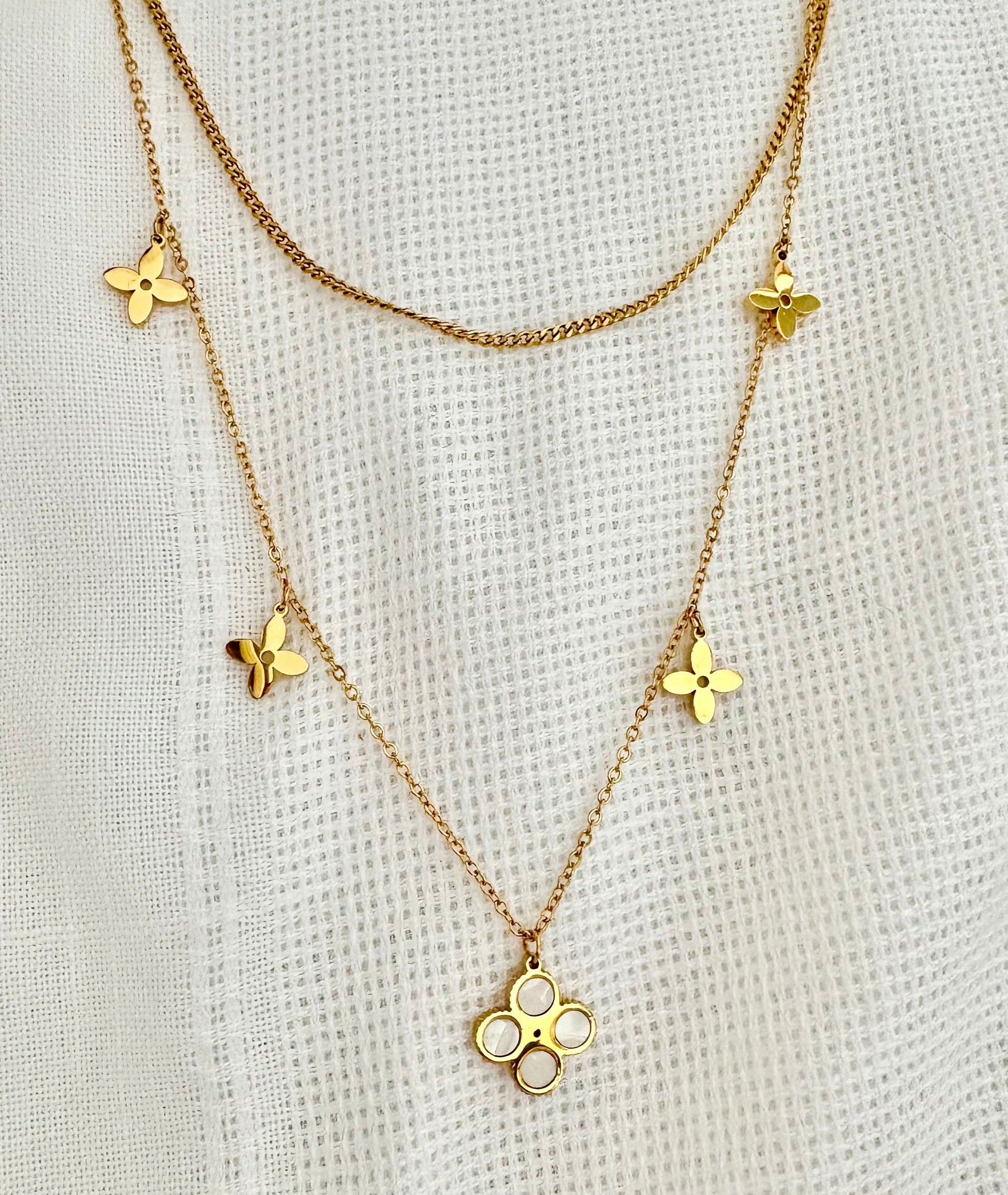 Gold necklace with floral pendants on a textured beige background