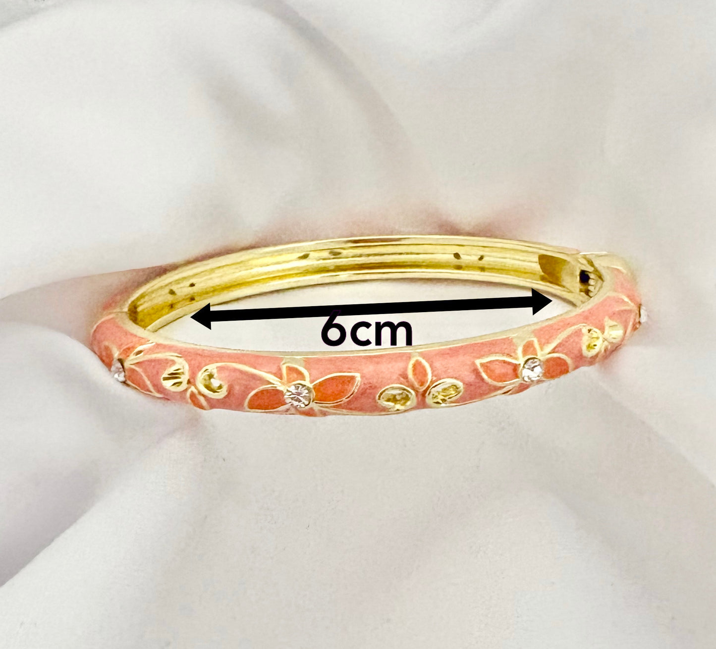 Pink bangle with gold accents on a white fabric background, showing measurement of 6cm.