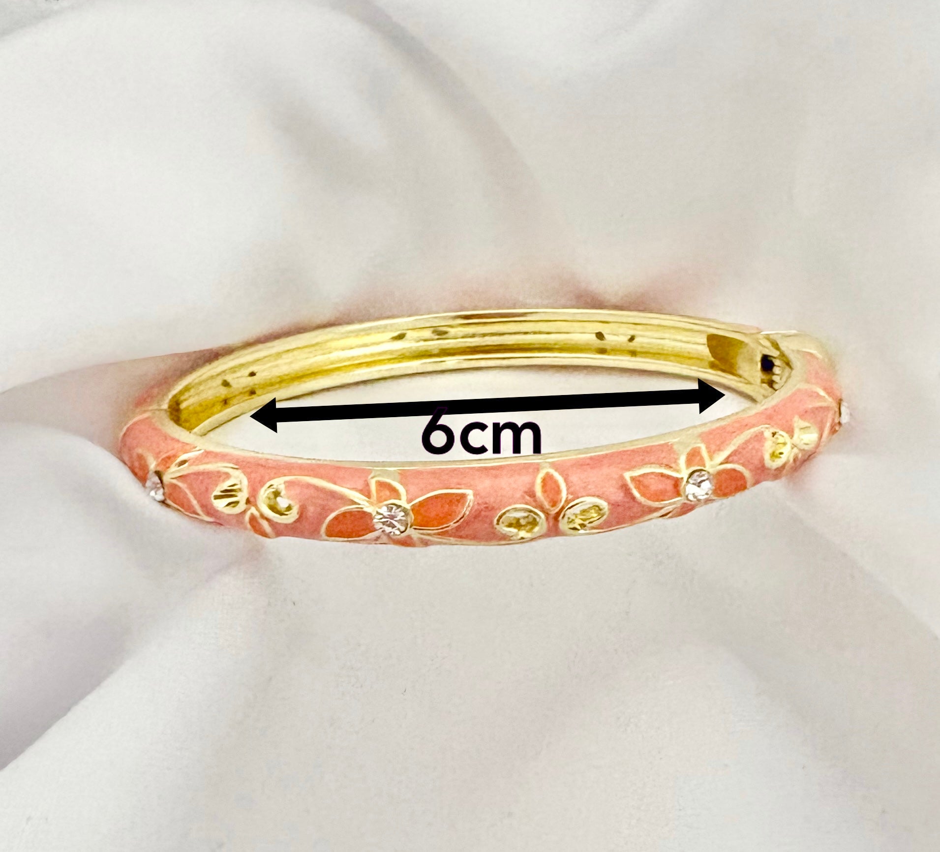 Pink bangle with gold accents on a white fabric background, showing measurement of 6cm.