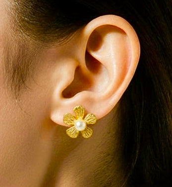 Close-up of an ear wearing a gold flower-shaped earring with a pearl center.