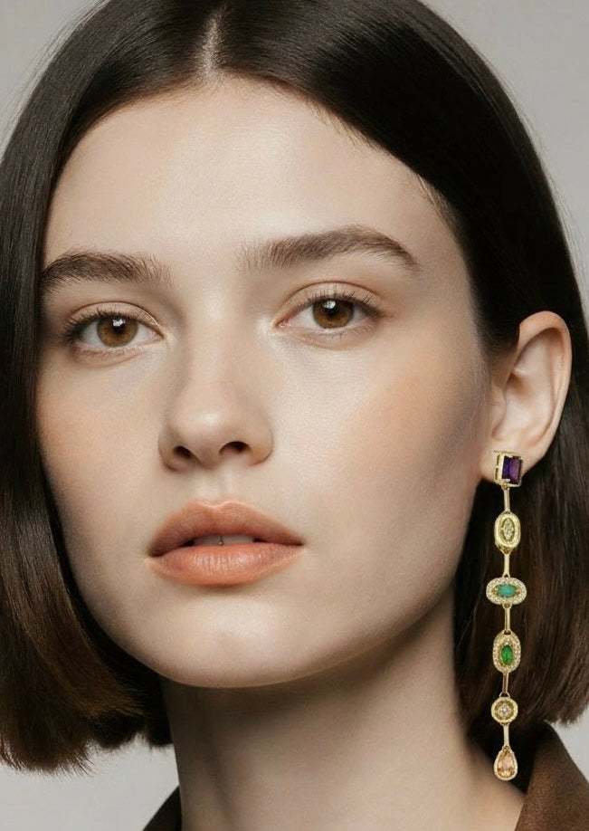 Close-up of a woman wearing a gold earring with gemstones on a neutral background