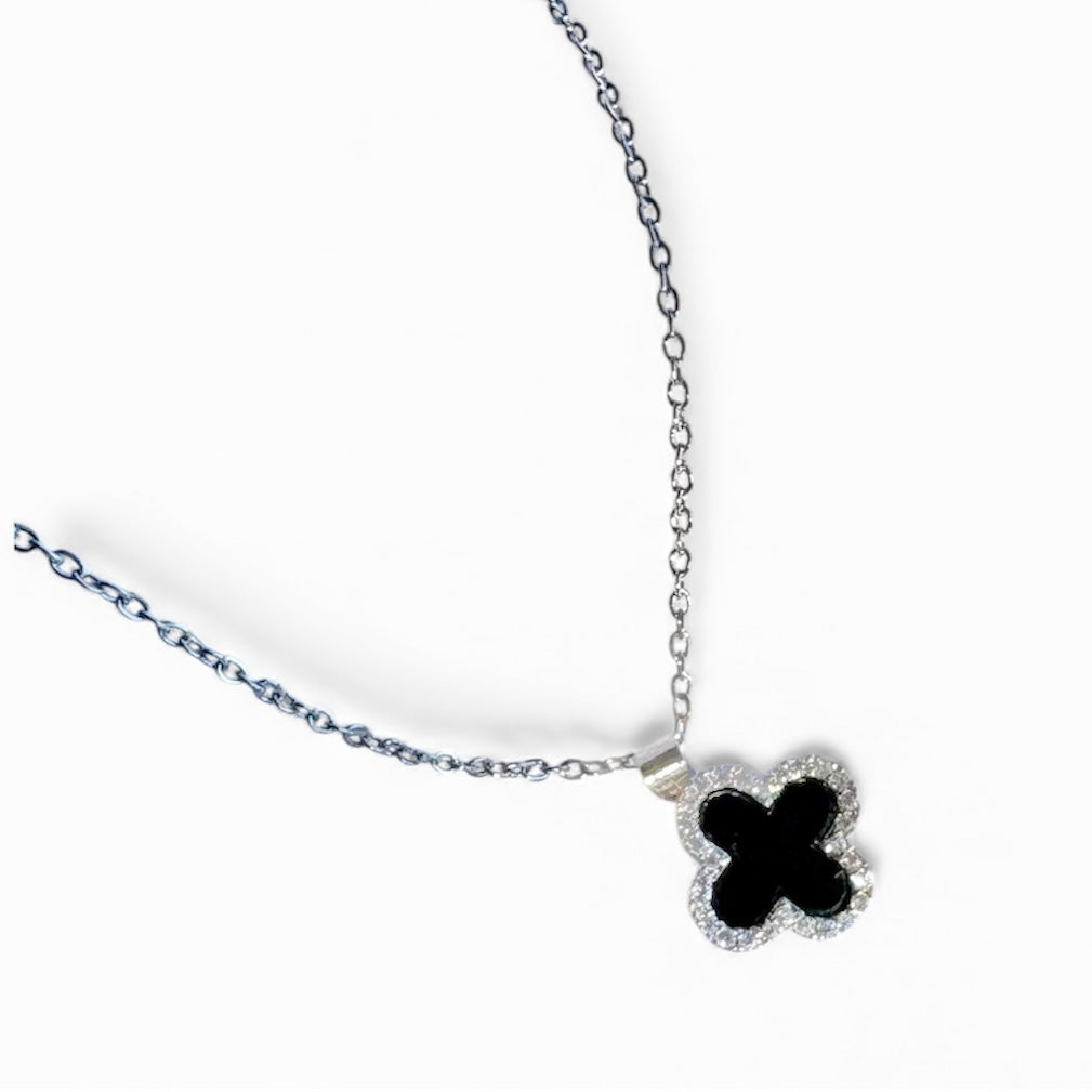 Silver necklace with black clover pendant on white satin background.