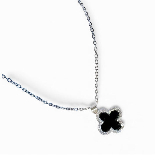 Silver necklace with black clover pendant on white satin background.
