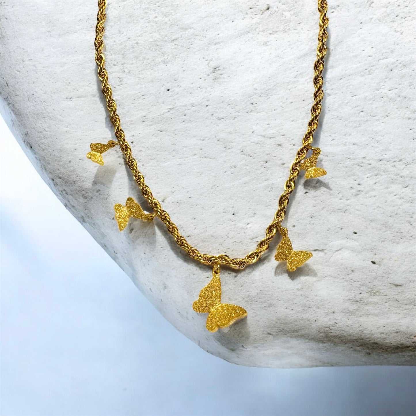 Gold butterfly necklace on a textured stone surface